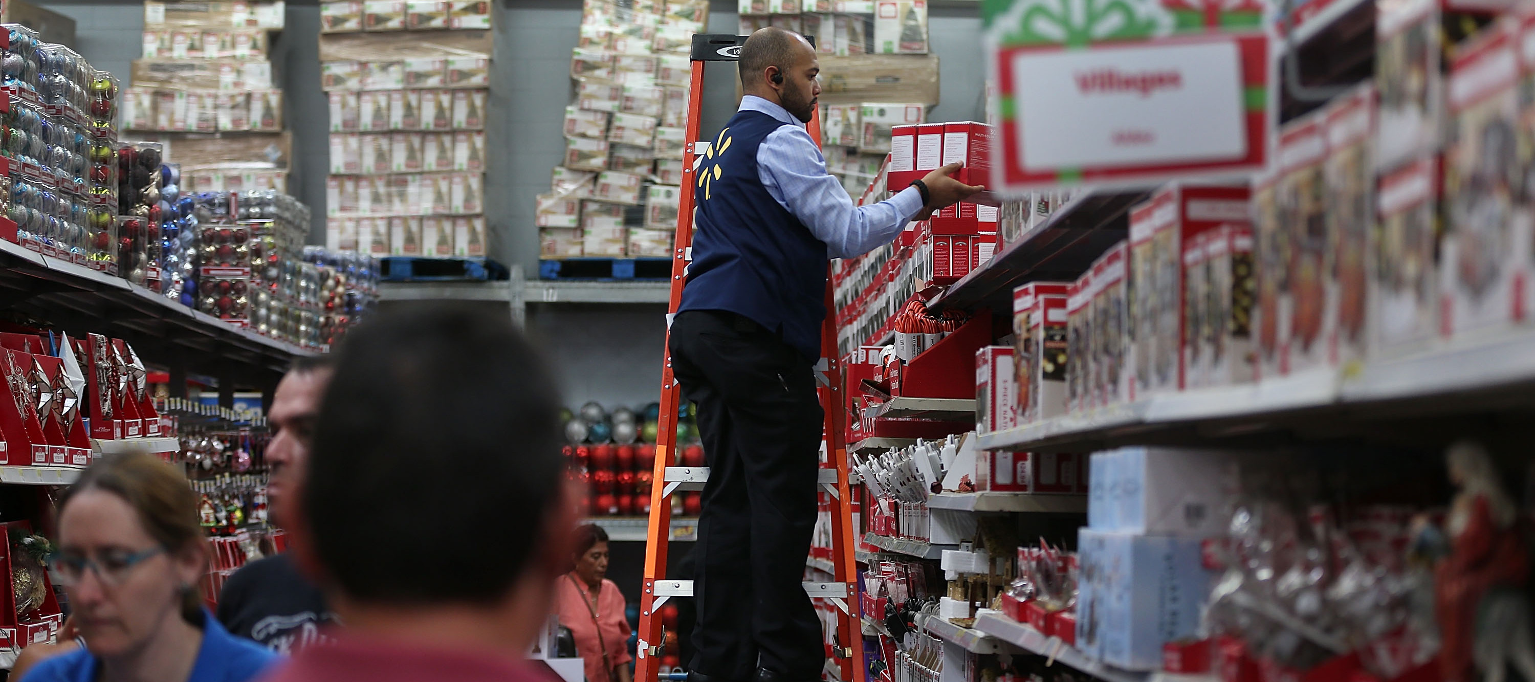 A Walmart employee stands on a ladder and puts out Christmas items.