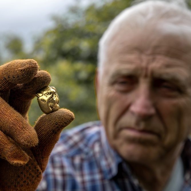 A photo of an elderly man holding a nugget of gold
