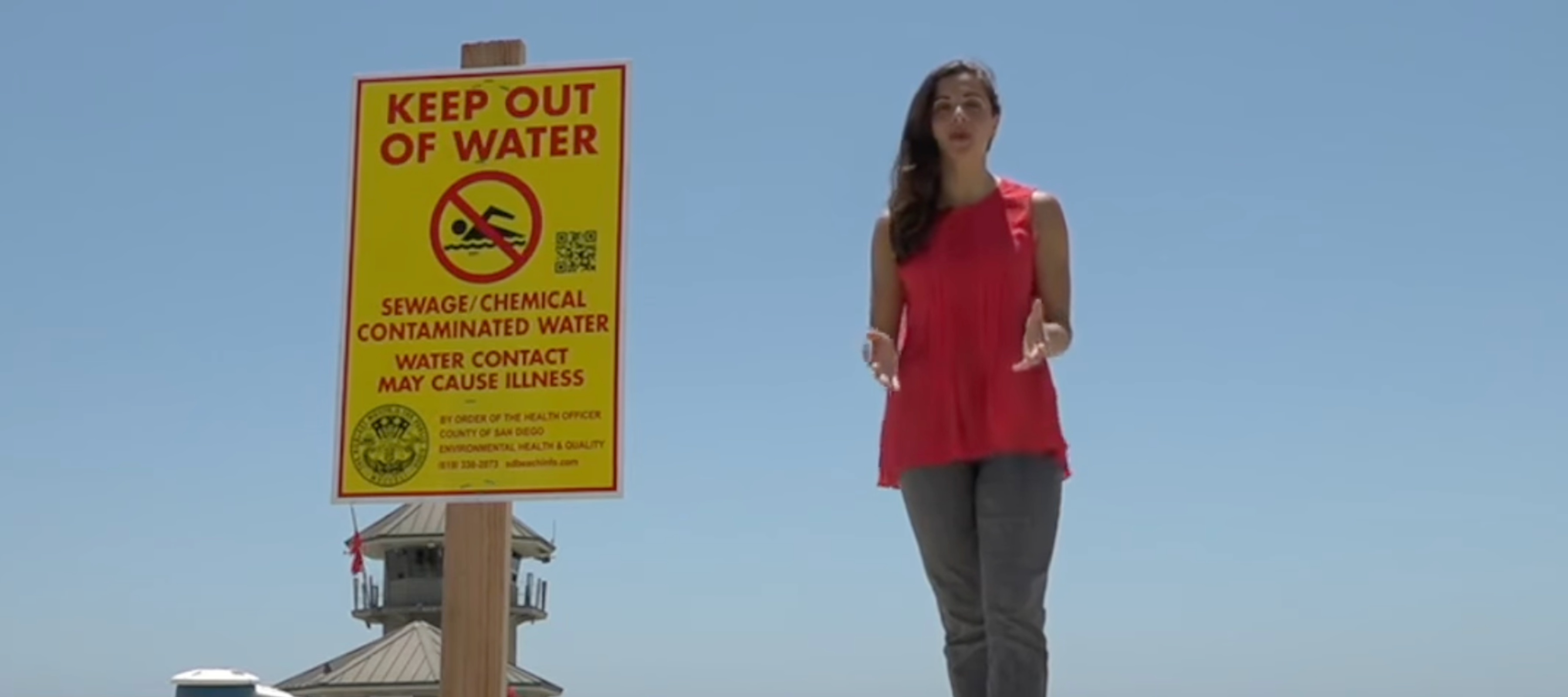 Photo of reporter on Coronado Beach with "Keep Out of Water" sign