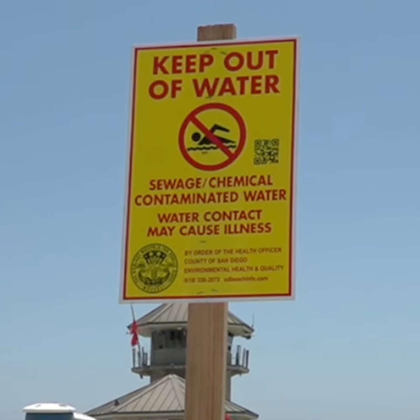 Photo of reporter on Coronado Beach with "Keep Out of Water" sign