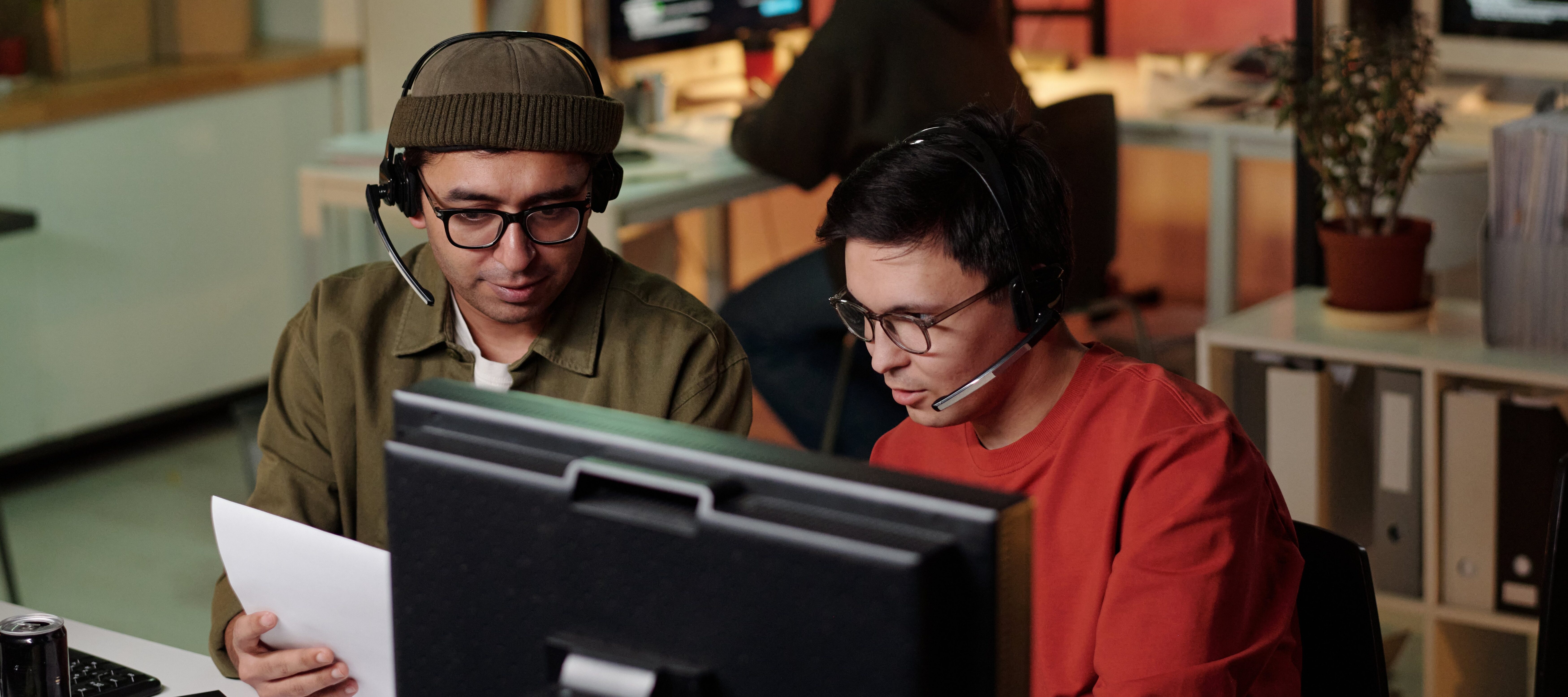 Two young male tech workers discussing work at computer desk