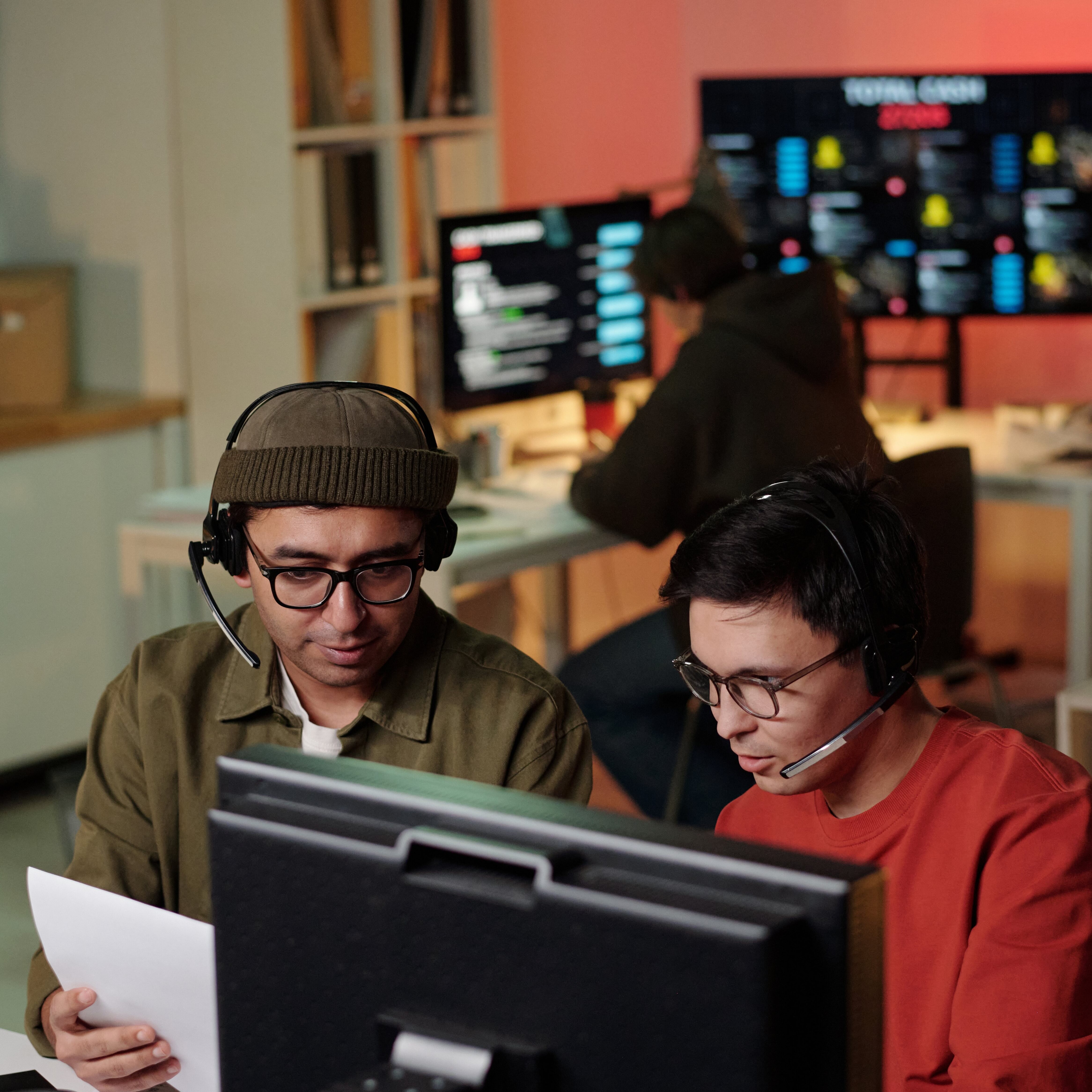 Two young male tech workers discussing work at computer desk