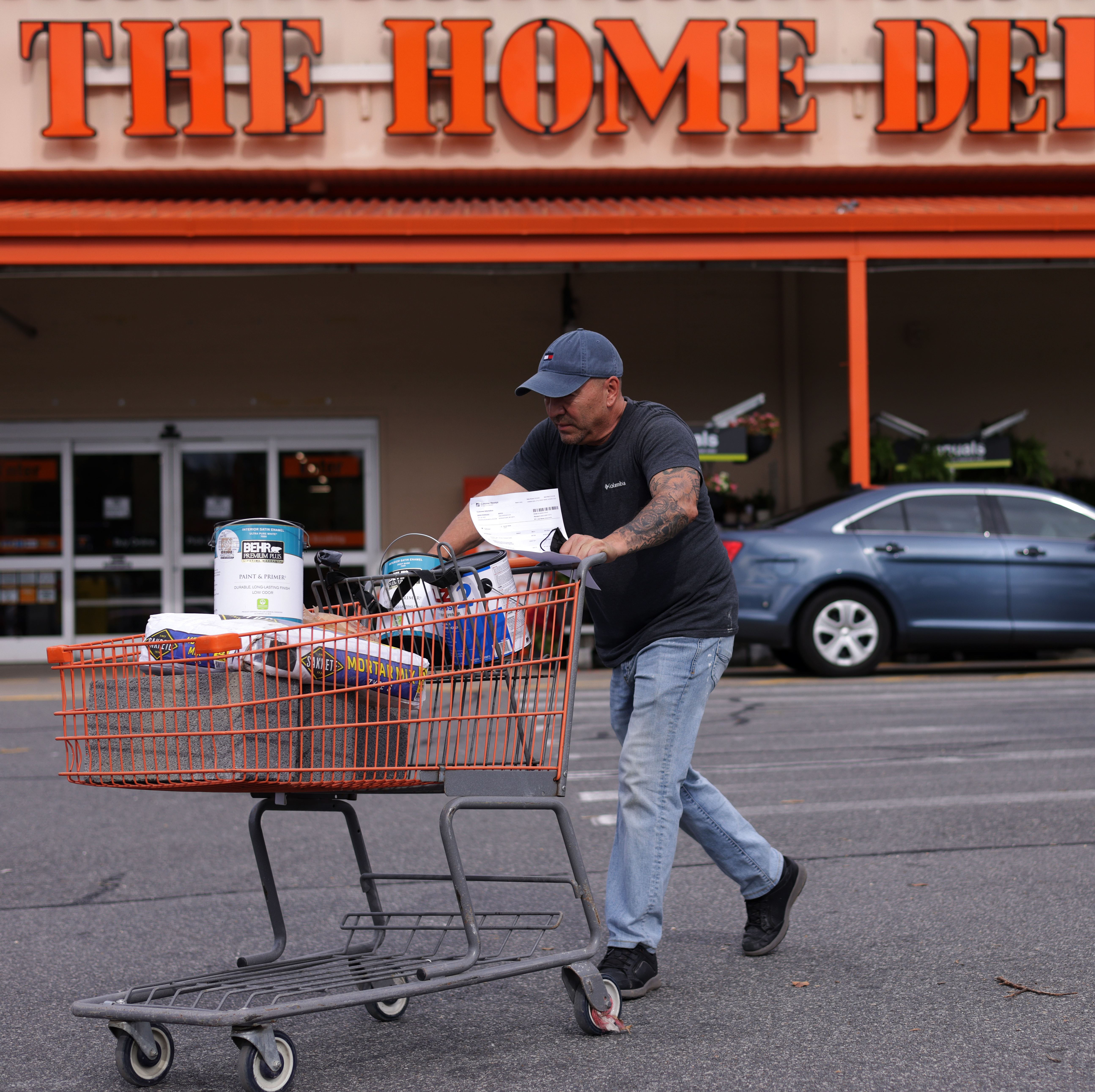 A shopper leaves a Home Depot with merchandise in a shopping cart.