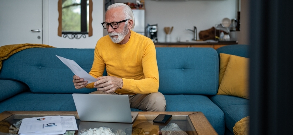 Photo of older man in front of laptop looking at papers