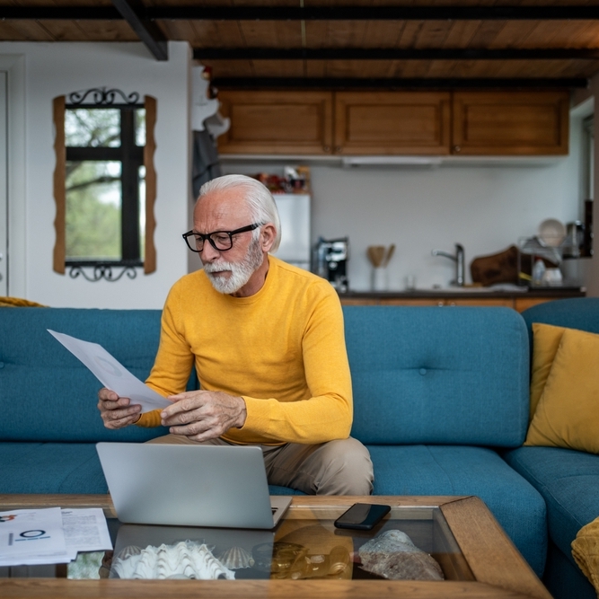 Photo of older man in front of laptop looking at papers