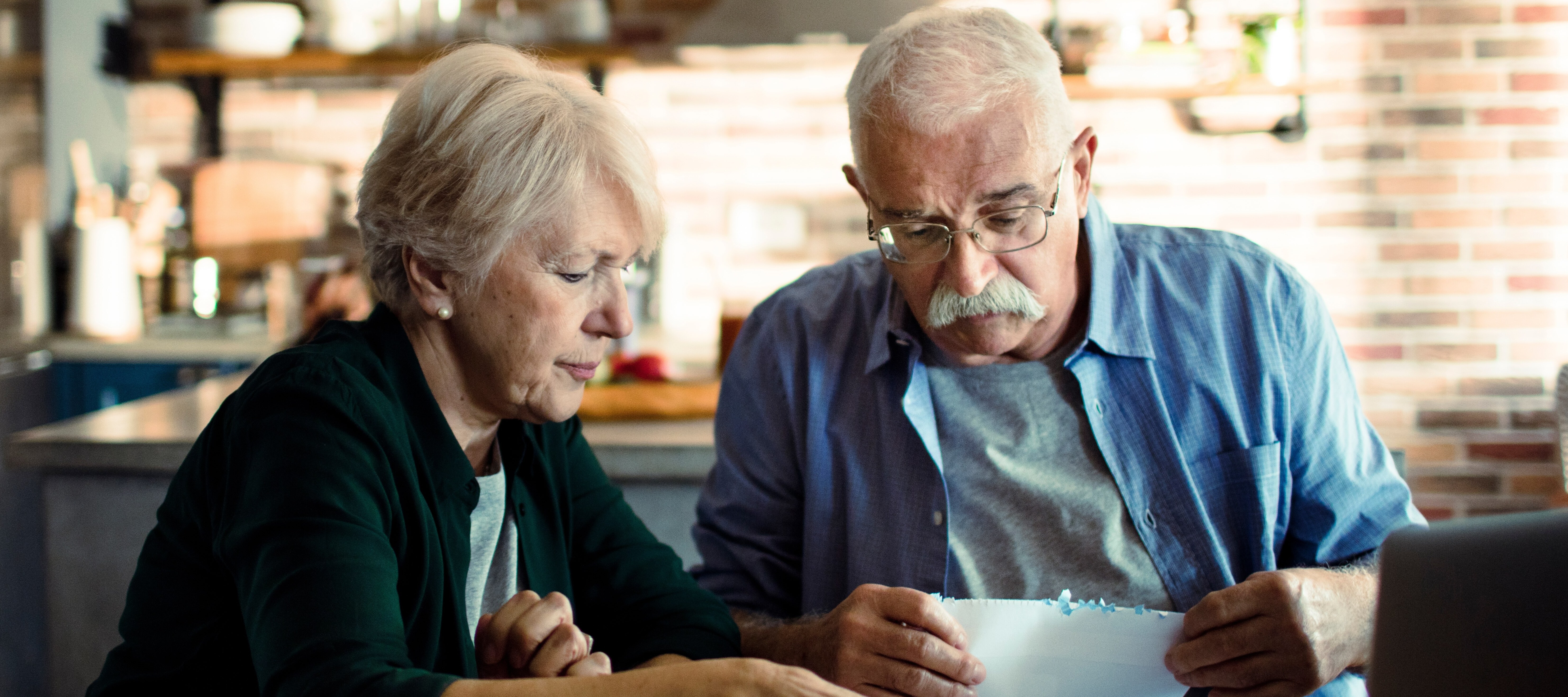 An older couple sit at their kitchen table and sort through papers.