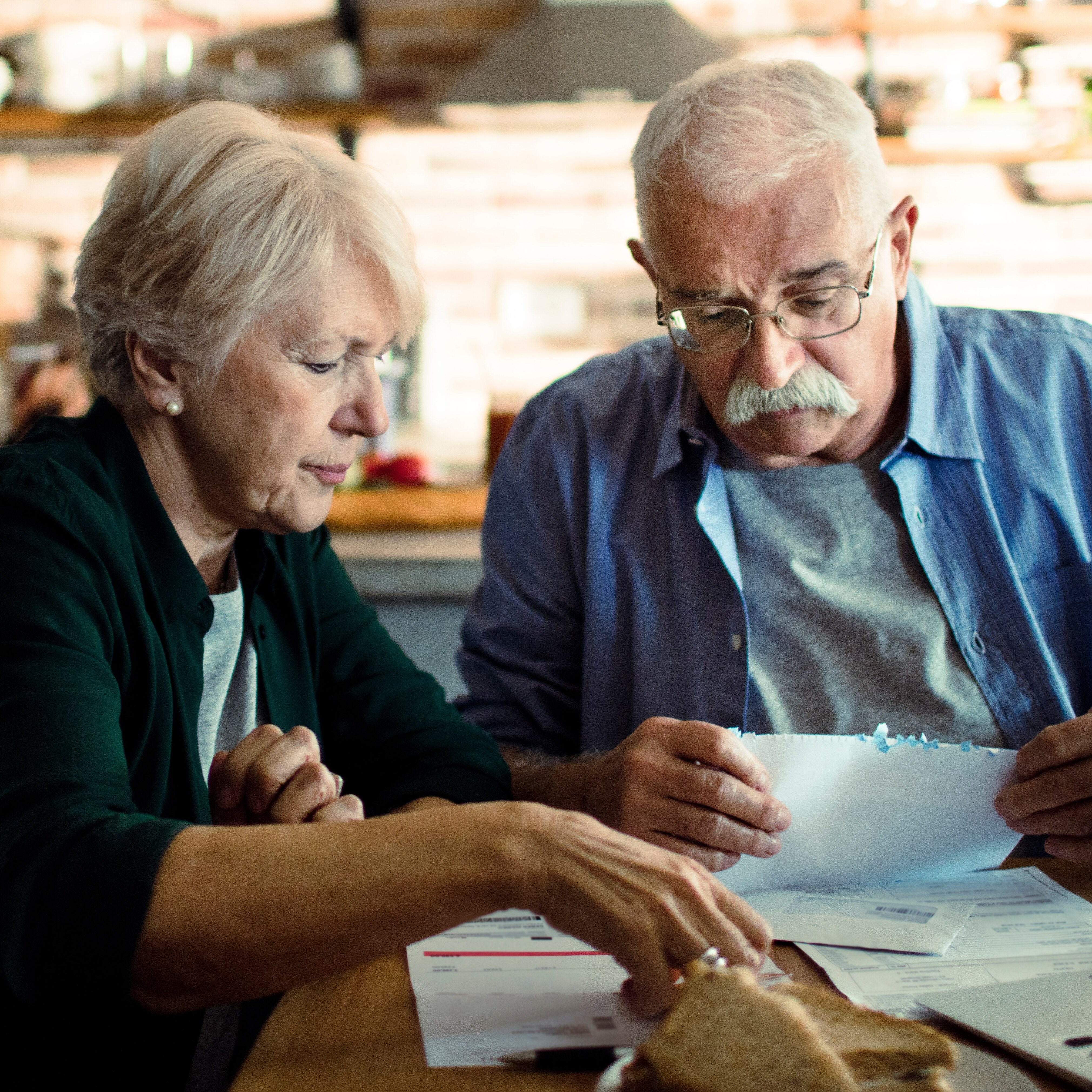 An older couple sit at their kitchen table and sort through papers.
