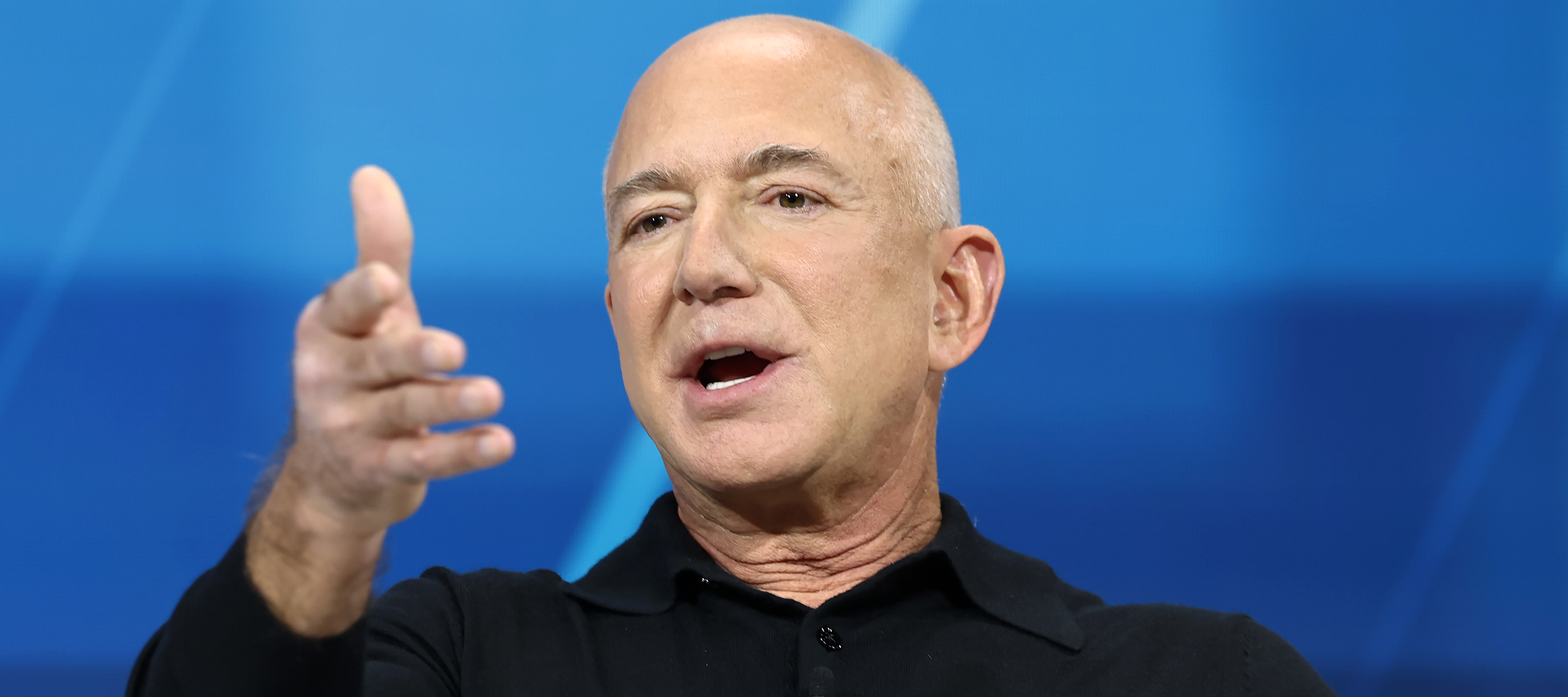 A close up of founder and chairman of Amazon Jeff Bezos speaking on stage and holding his hand up in the air.