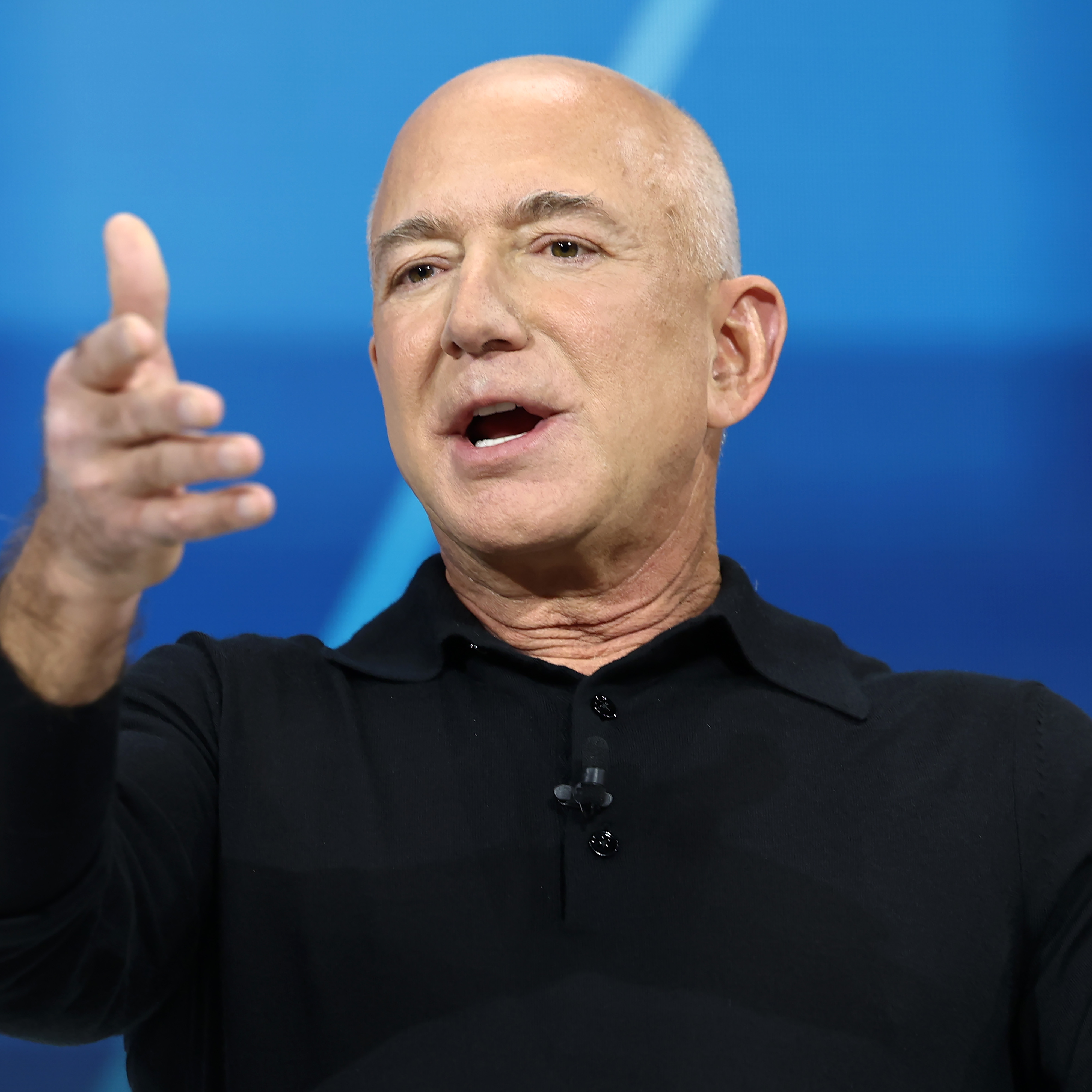 A close up of founder and chairman of Amazon Jeff Bezos speaking on stage and holding his hand up in the air.