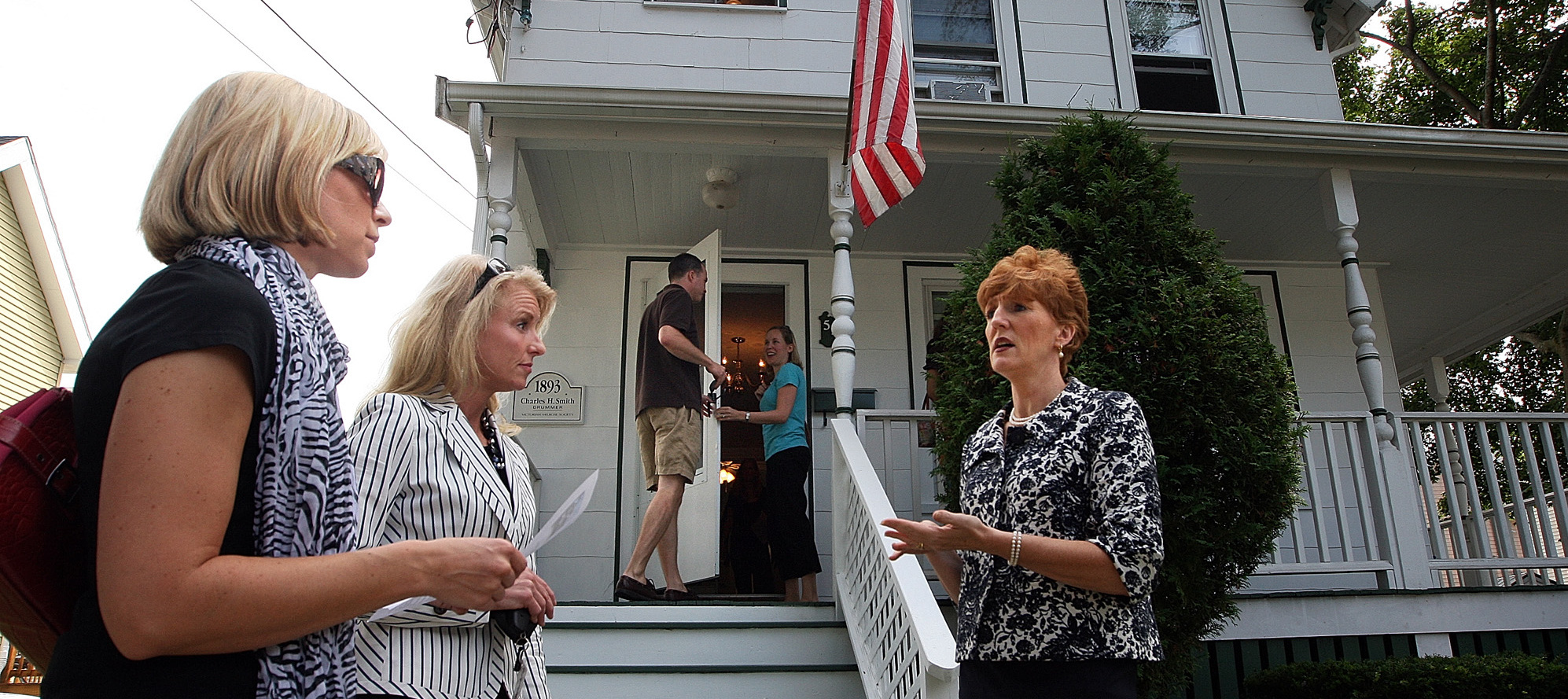 Prospective buyers speak with a real estate agent in front of a home.