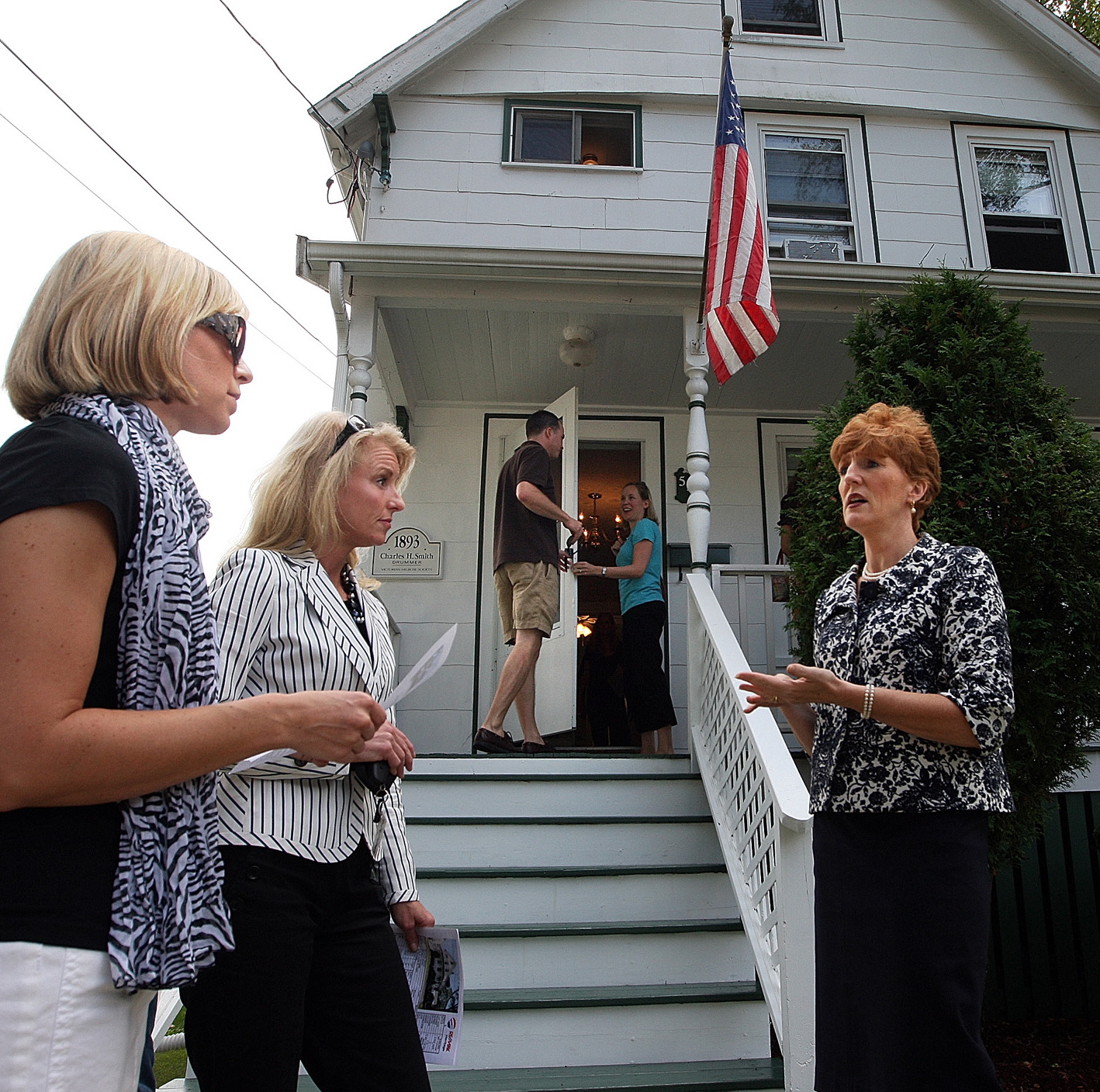 Prospective buyers speak with a real estate agent in front of a home.