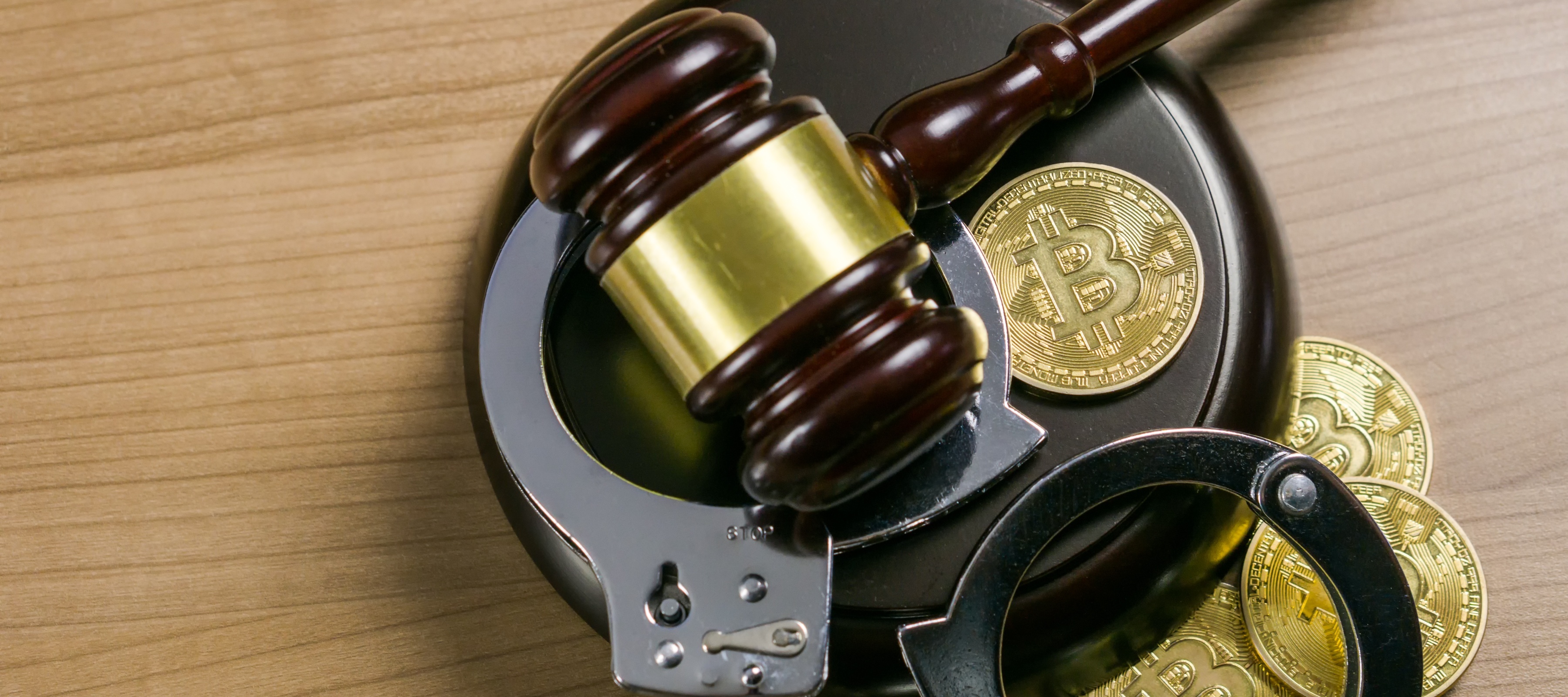 A judge's gavel pictured with handcuffs and gold coins strewn about