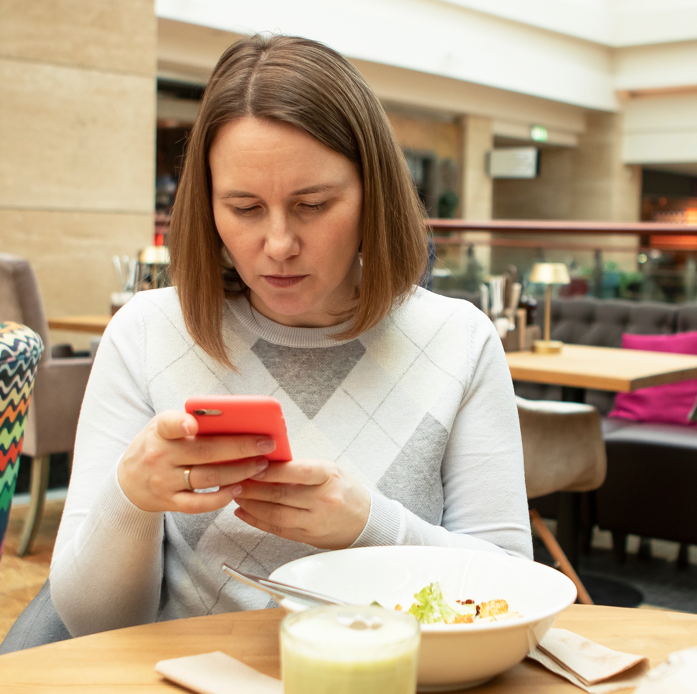 Young woman concernedly looking at phone while eating meal