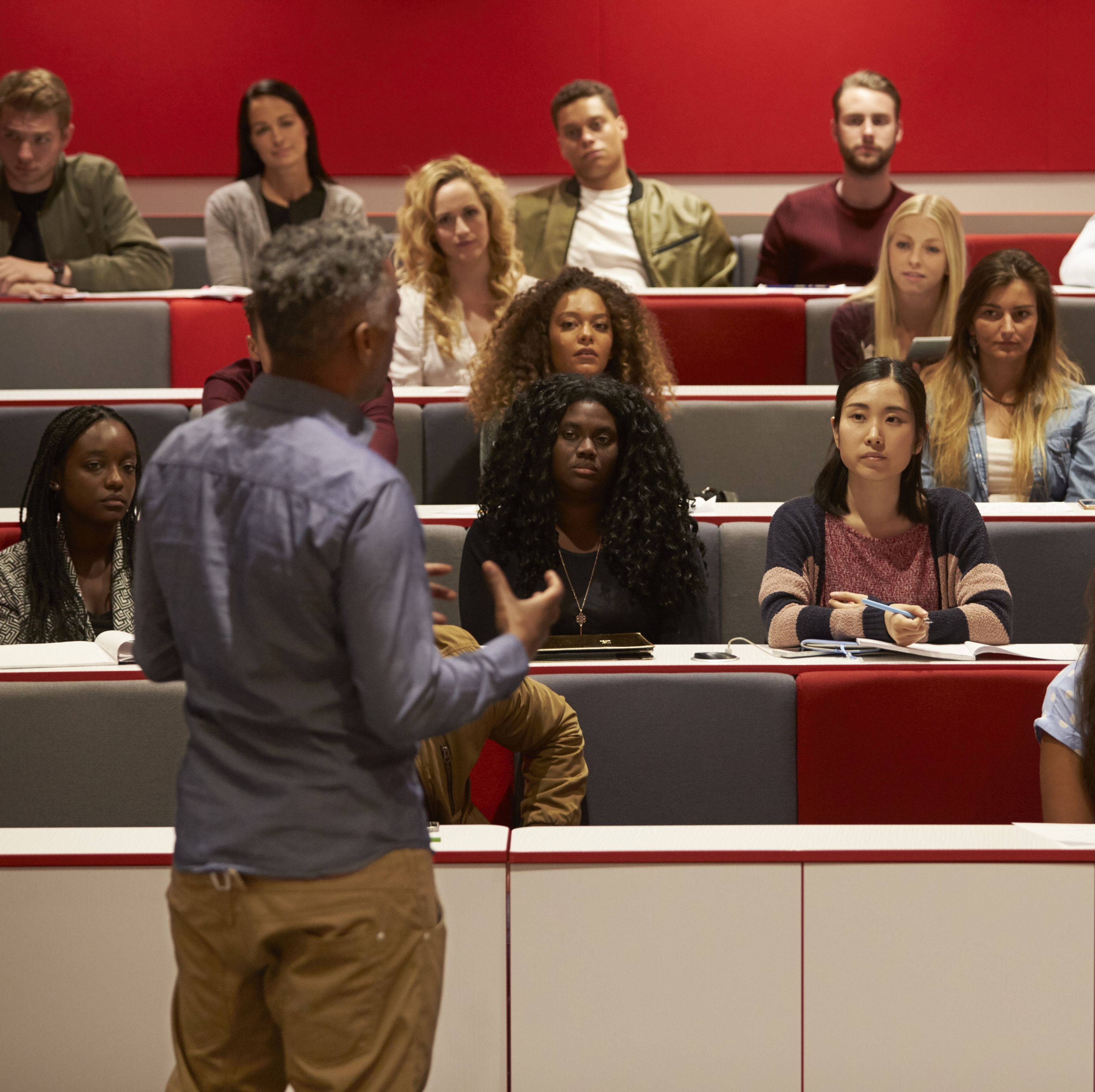 A group of students attentively listens to a professor in a lecture hall.