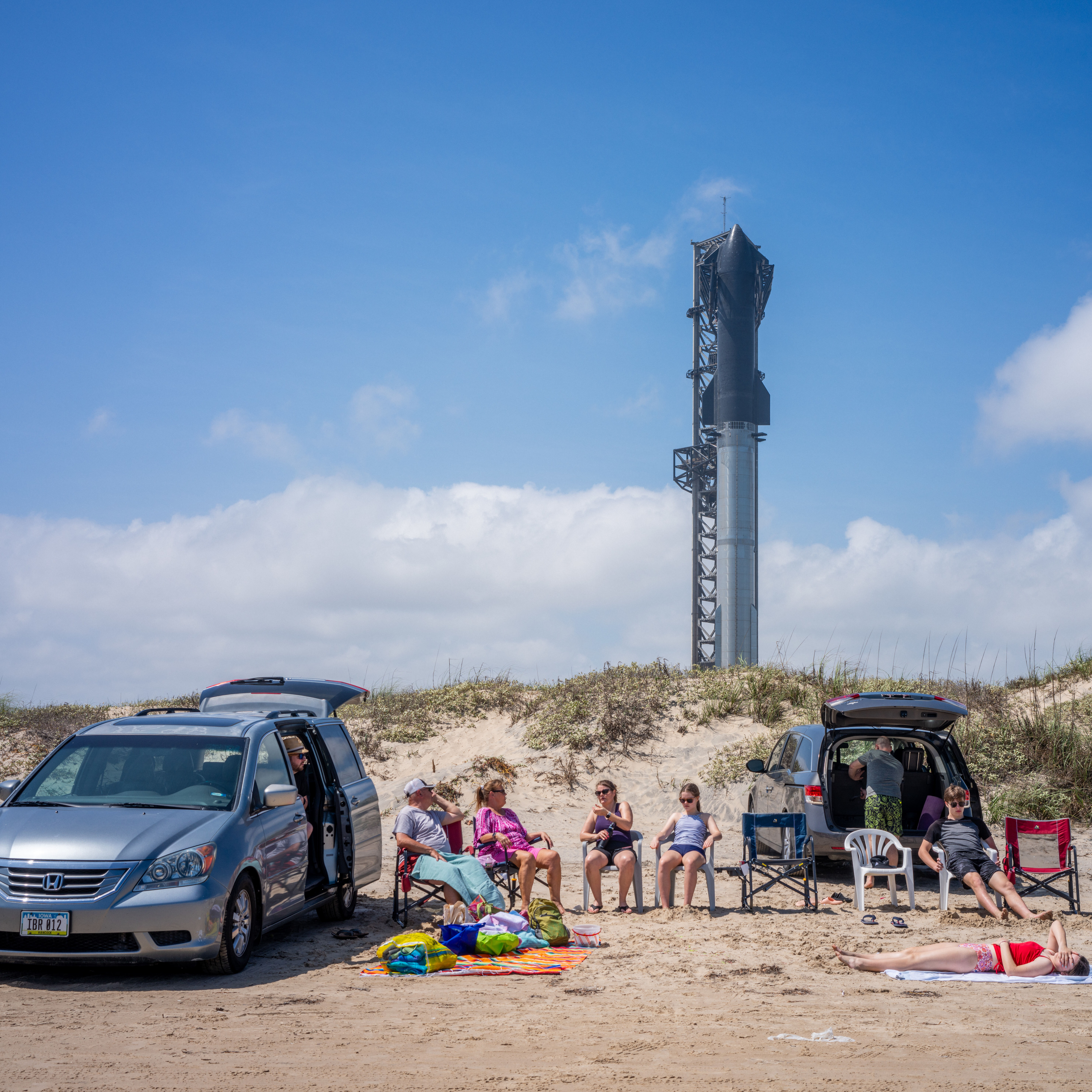 People spend time on the beach near the Starship Flight 3 Rocket a day before its scheduled launch.