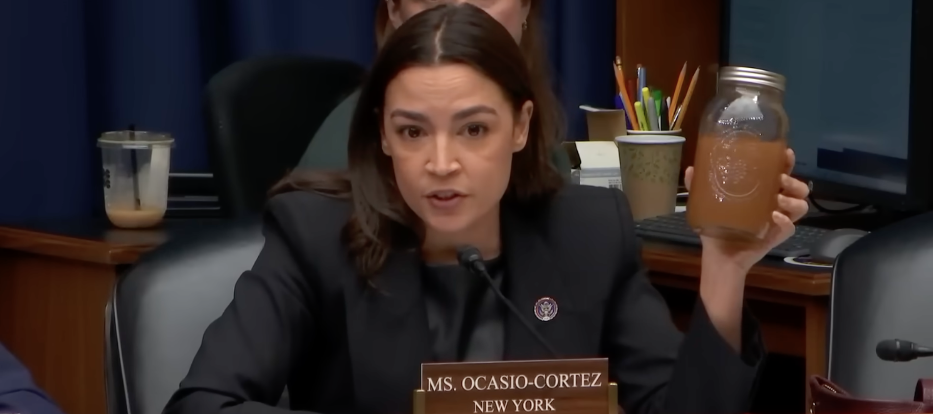Alexandria Ocasio-Cortez holds up a jar of brown water during a congressional hearing.