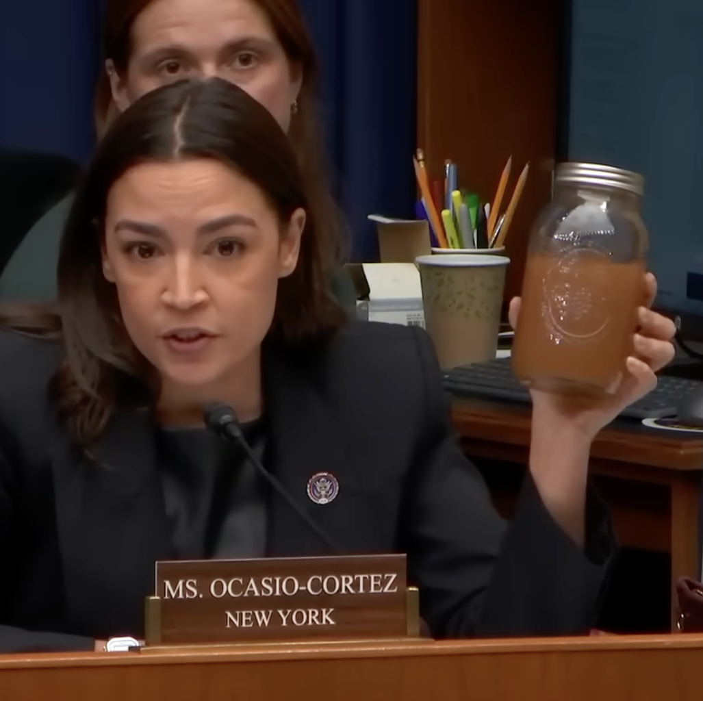 Alexandria Ocasio-Cortez holds up a jar of brown water during a congressional hearing.