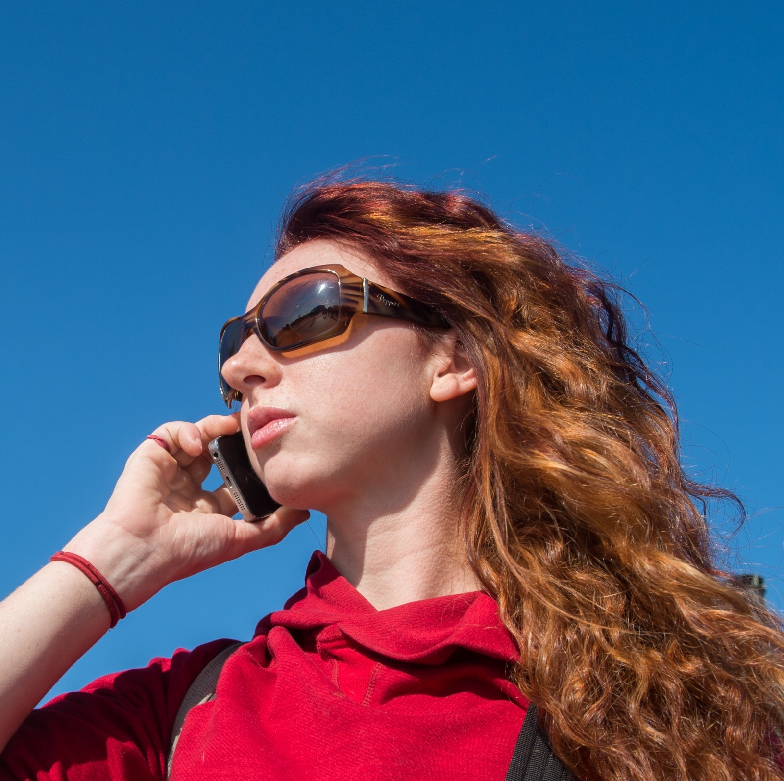 A redheaded woman wearing sunglasses speaks on her phone in front of Big Ben