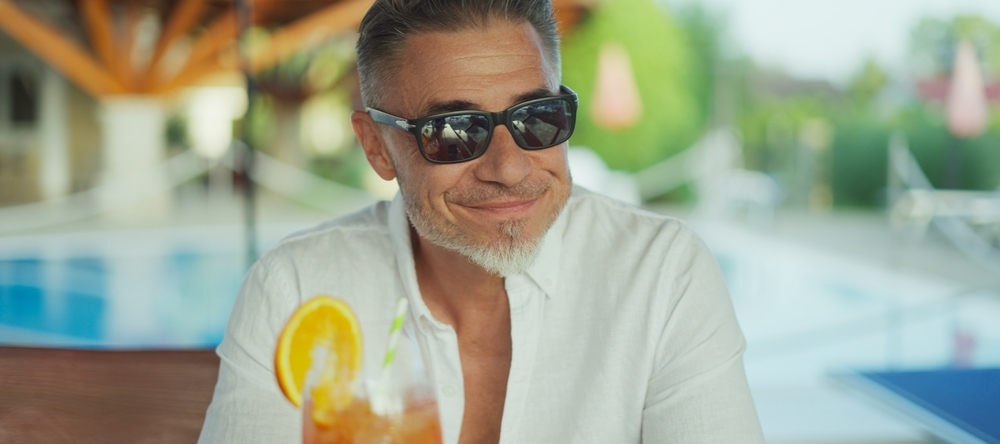 Mature man with sunglasses sitting by pool at hotel resort.