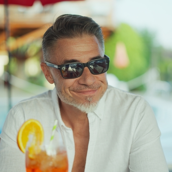 Mature man with sunglasses sitting by pool at hotel resort.