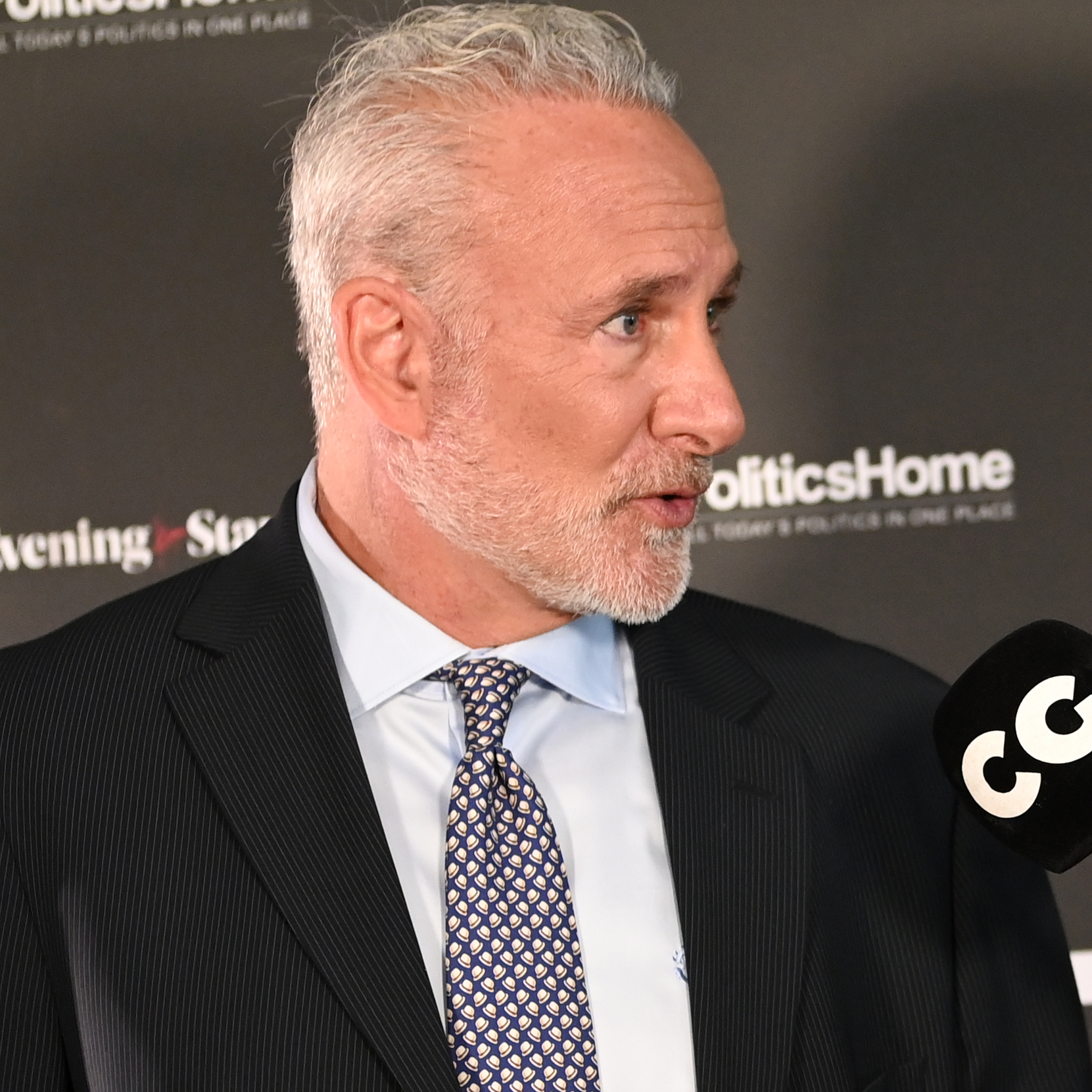 Peter Schiff speaks into a microphone wearing a black suit, blue dress shirt and speckled tie.