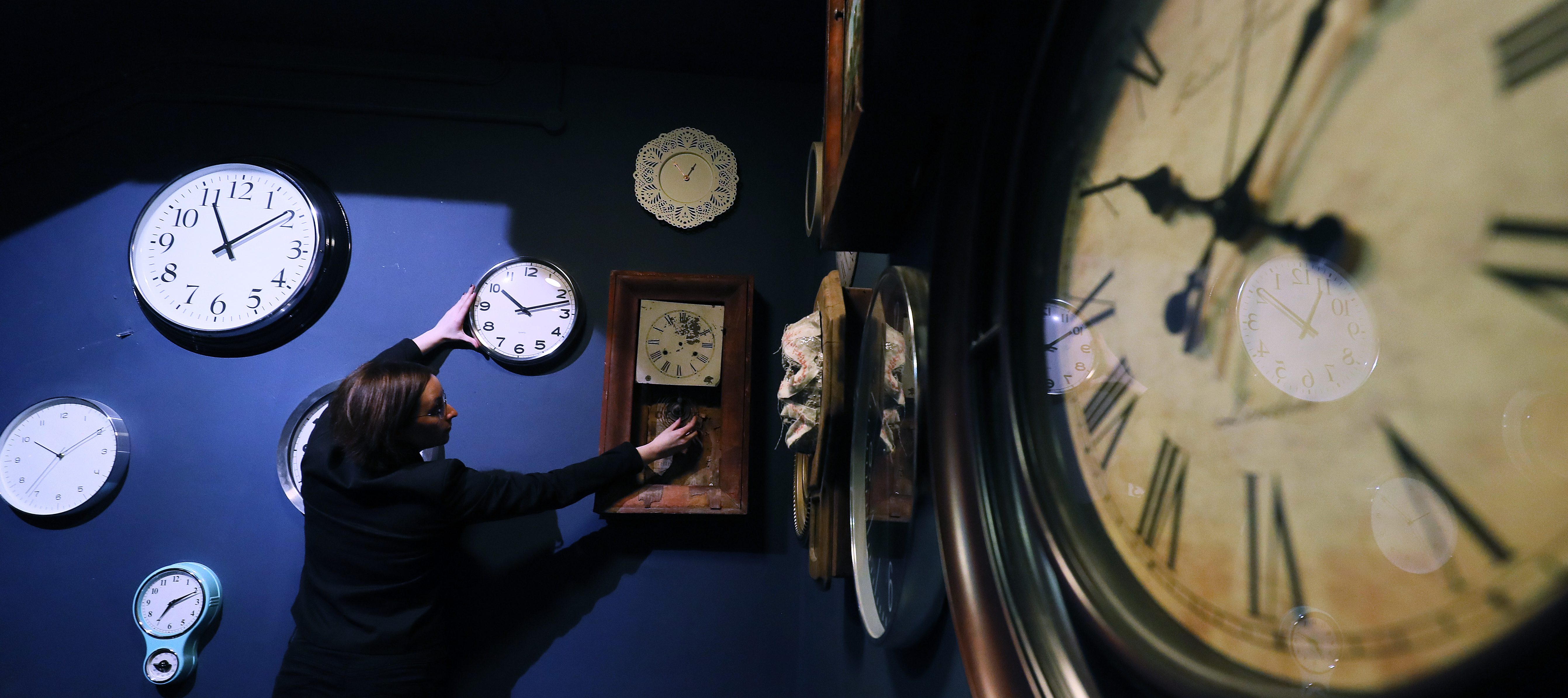 A woman adjust the clocks at the museum she works at.
