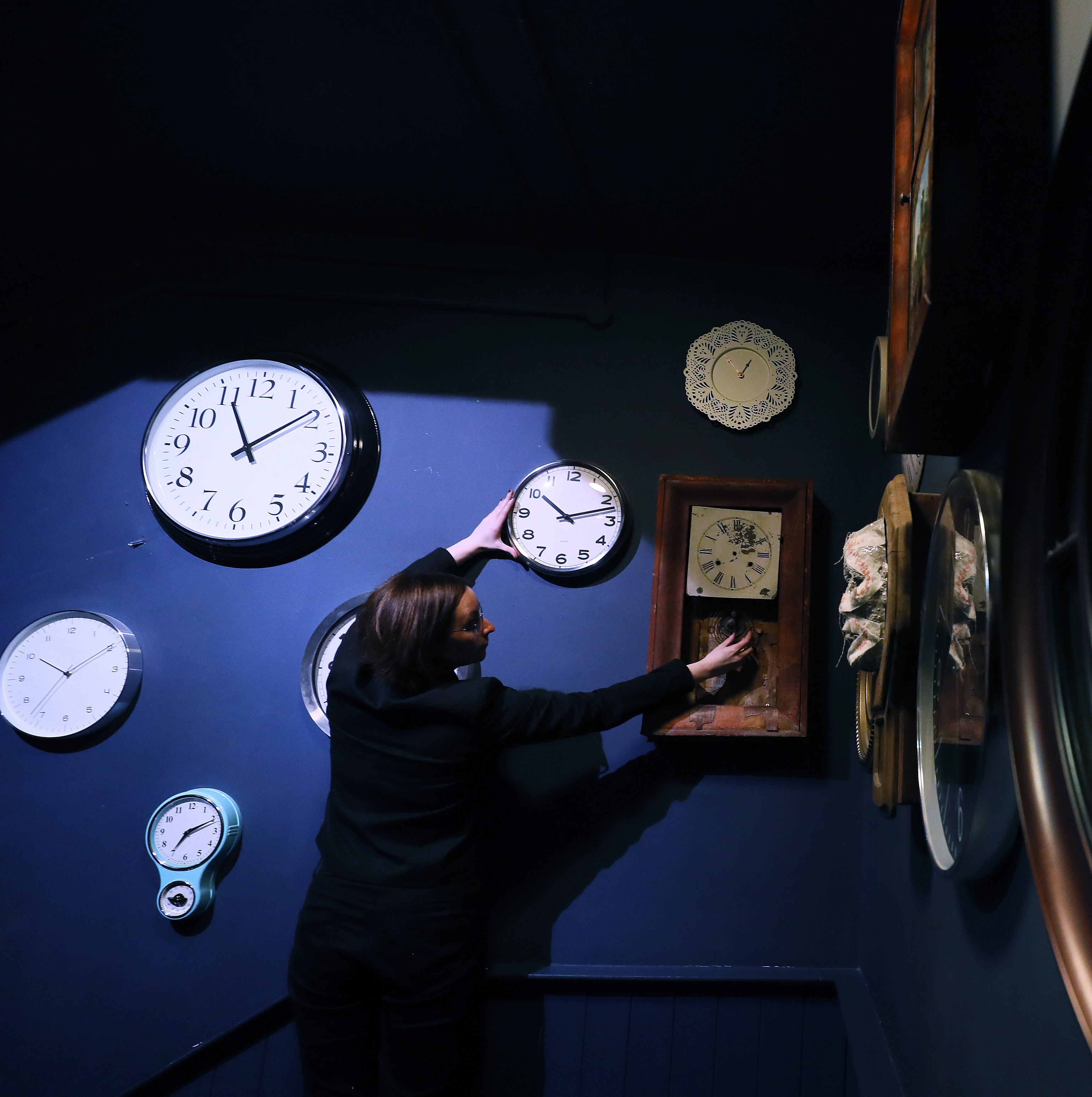 A woman adjust the clocks at the museum she works at.