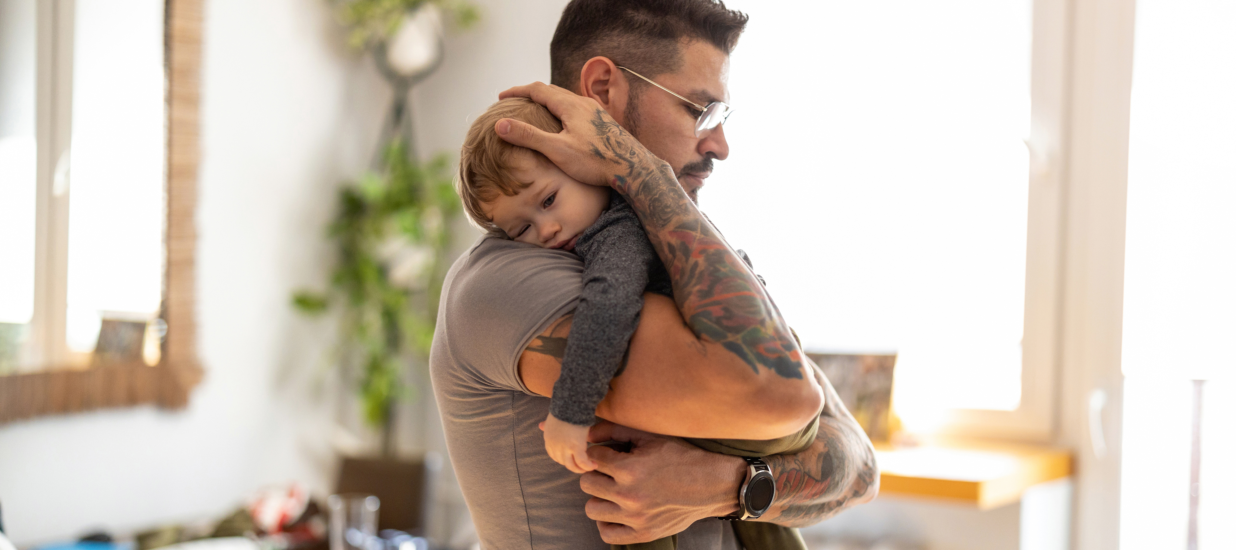 A young father holds his toddler in the middle of a living room.
