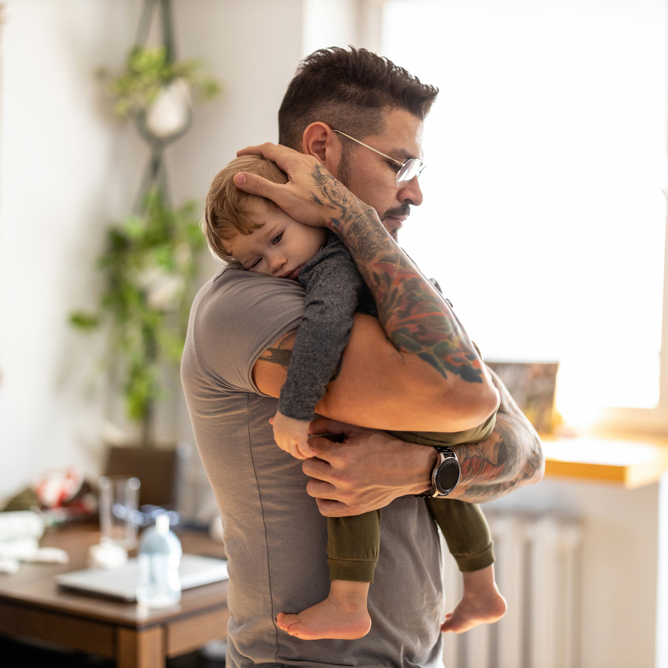 A young father holds his toddler in the middle of a living room.