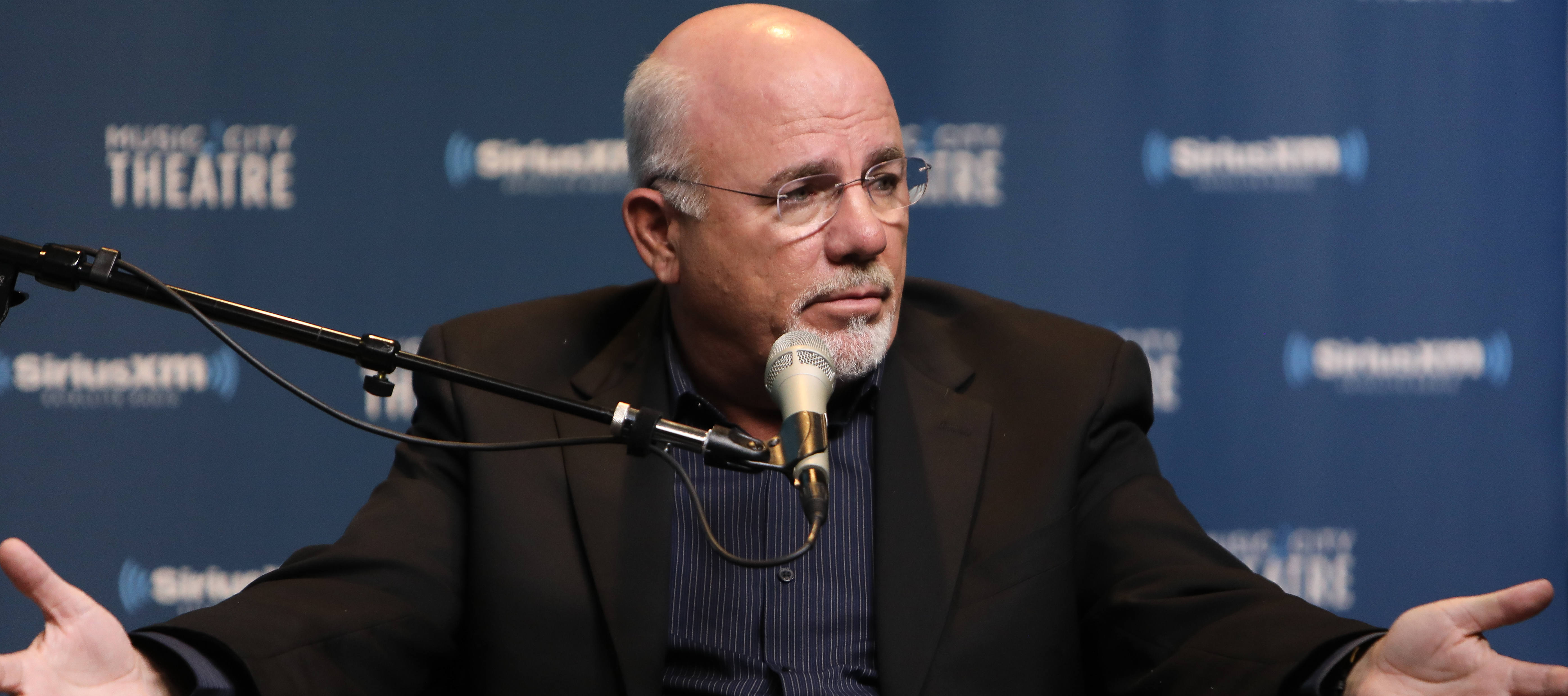 Dave Ramsey spreads both his hands out on stage, questioningly.