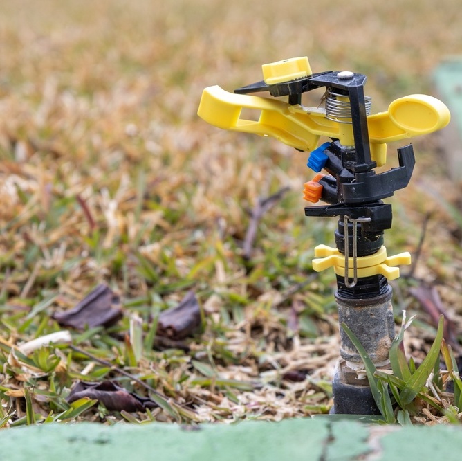 A photo of a sprinkler on a yellow lawn