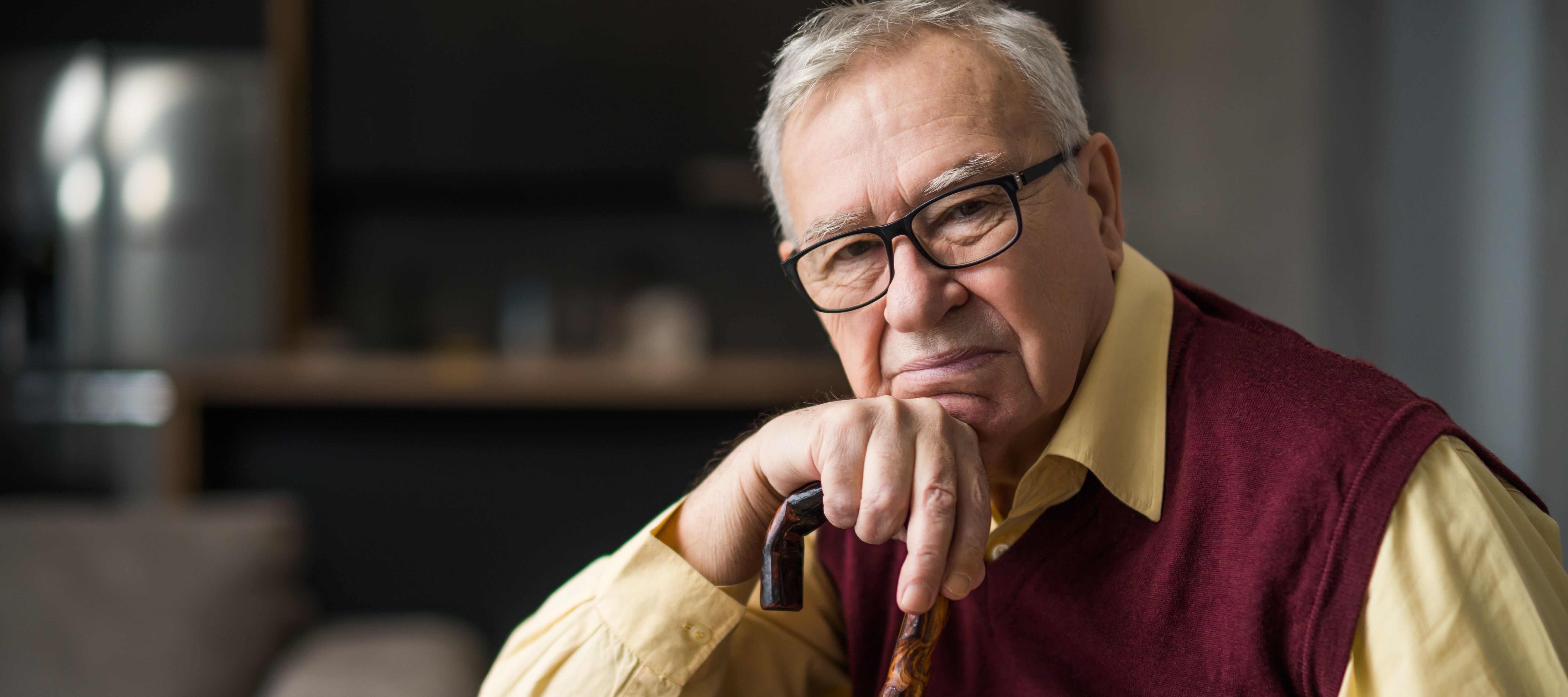 An older man with short, gray hair and glasses is resting on a cane.