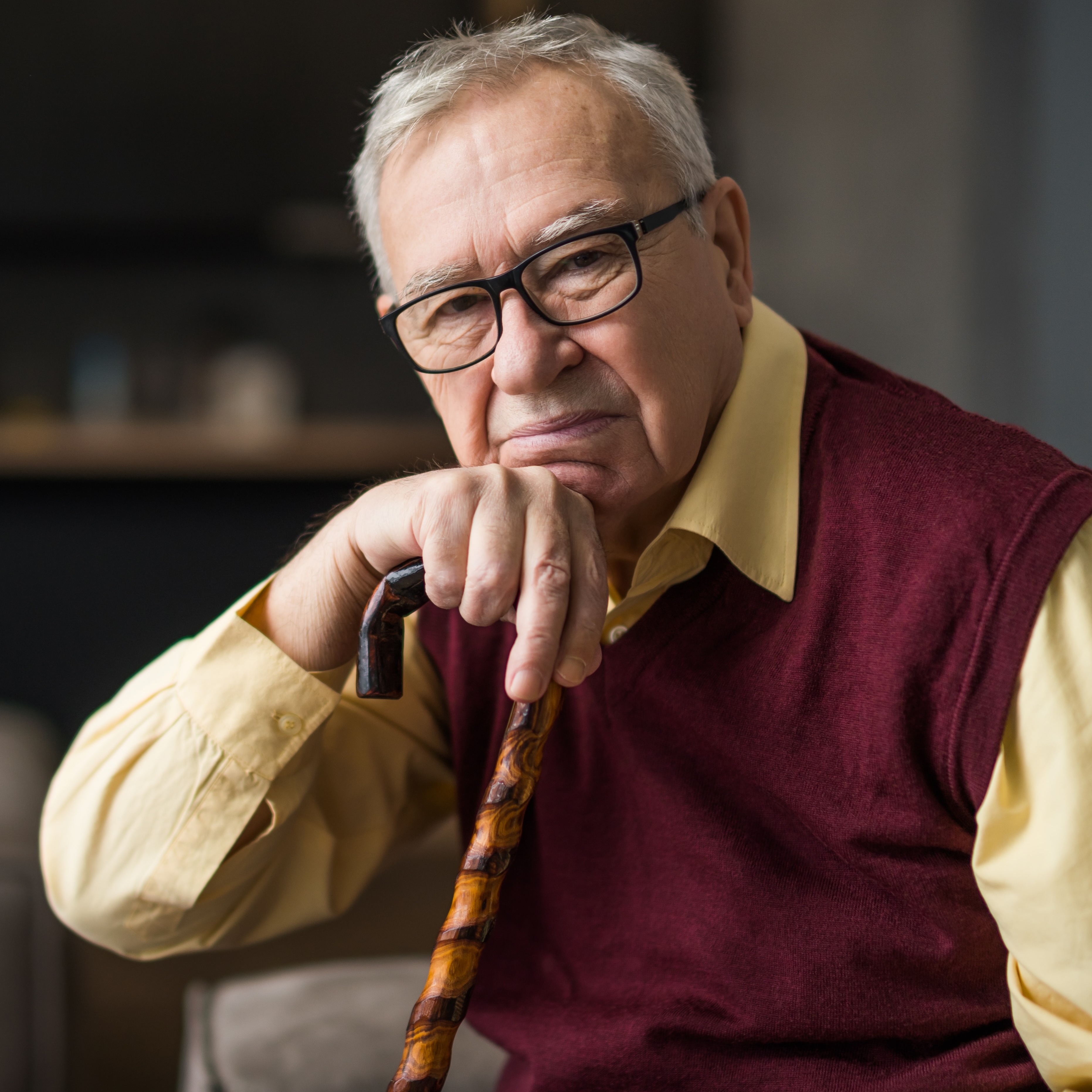 An older man with short, gray hair and glasses is resting on a cane.