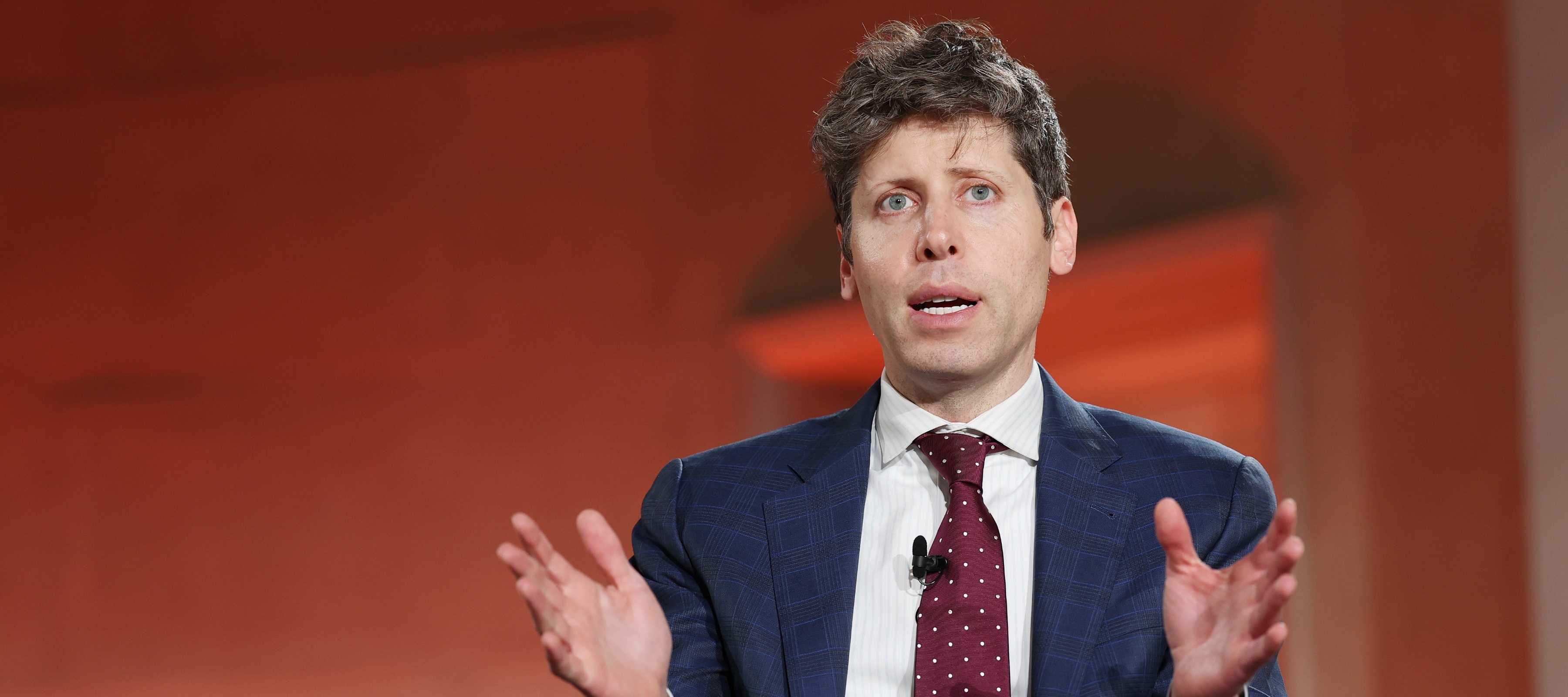 Sam Altman sits on stage with his hands open wide