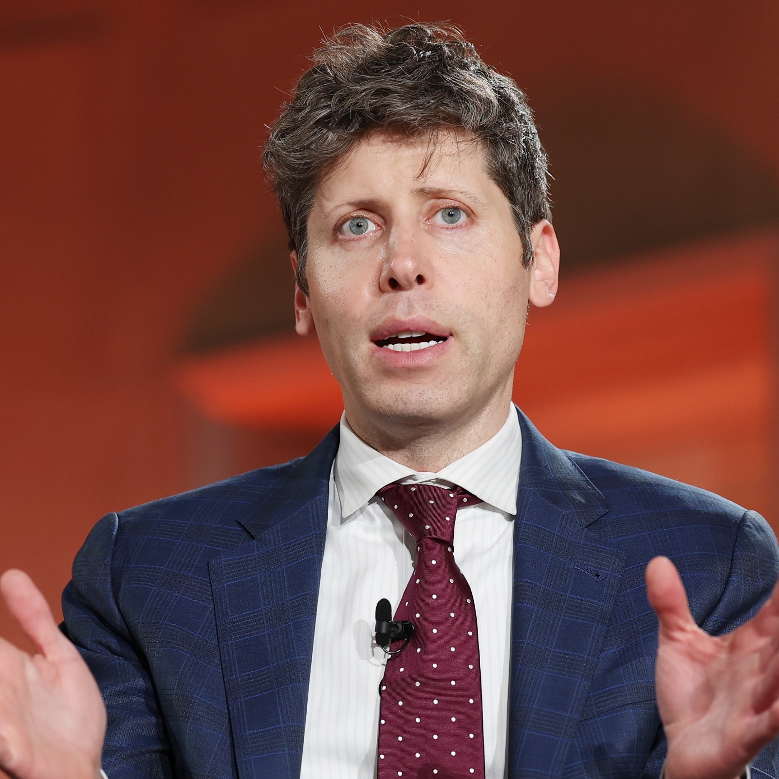 Sam Altman sits on stage with his hands open wide