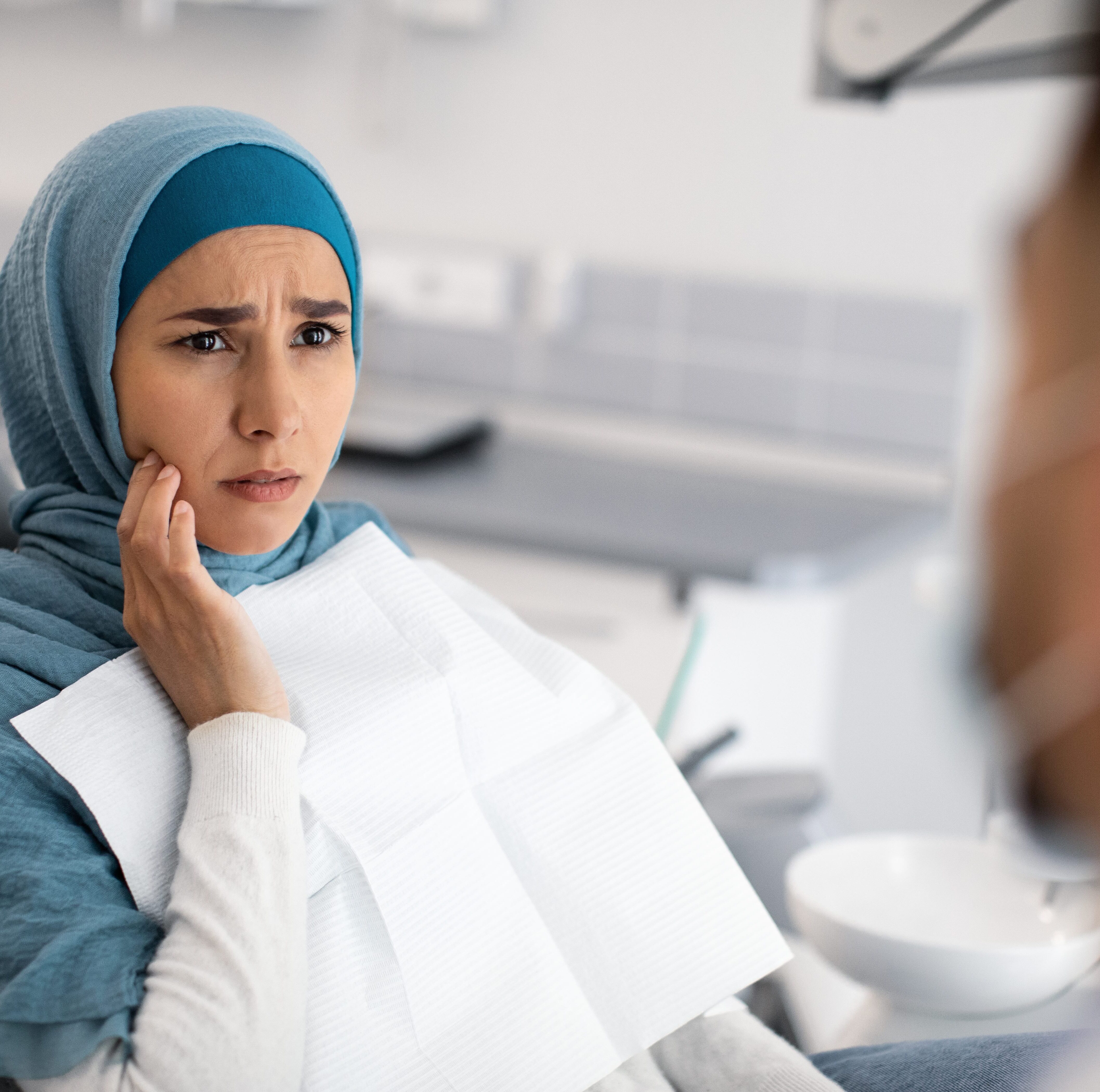 Young woman wearing blue headscarf looking concerned at dentist