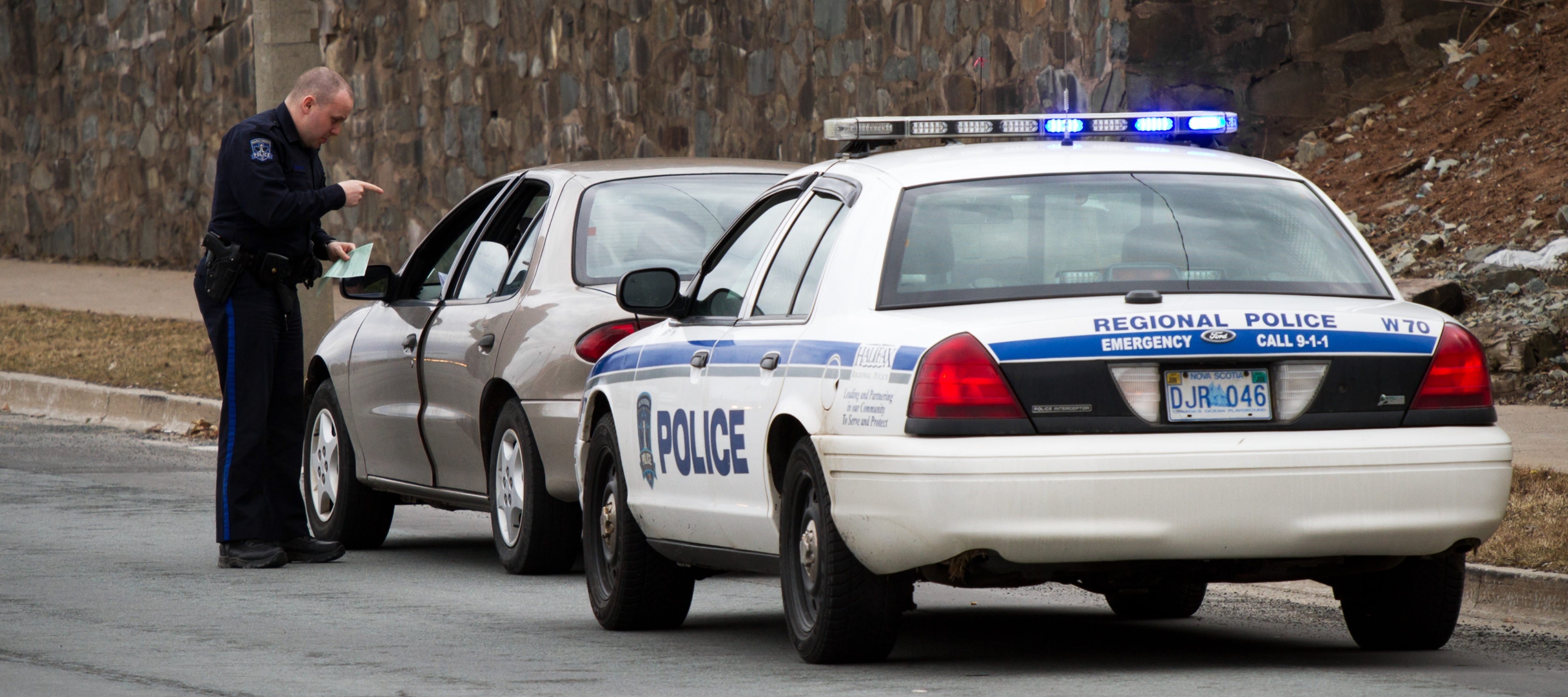 A fat bald police officer talking to a driver of a car he pulled over