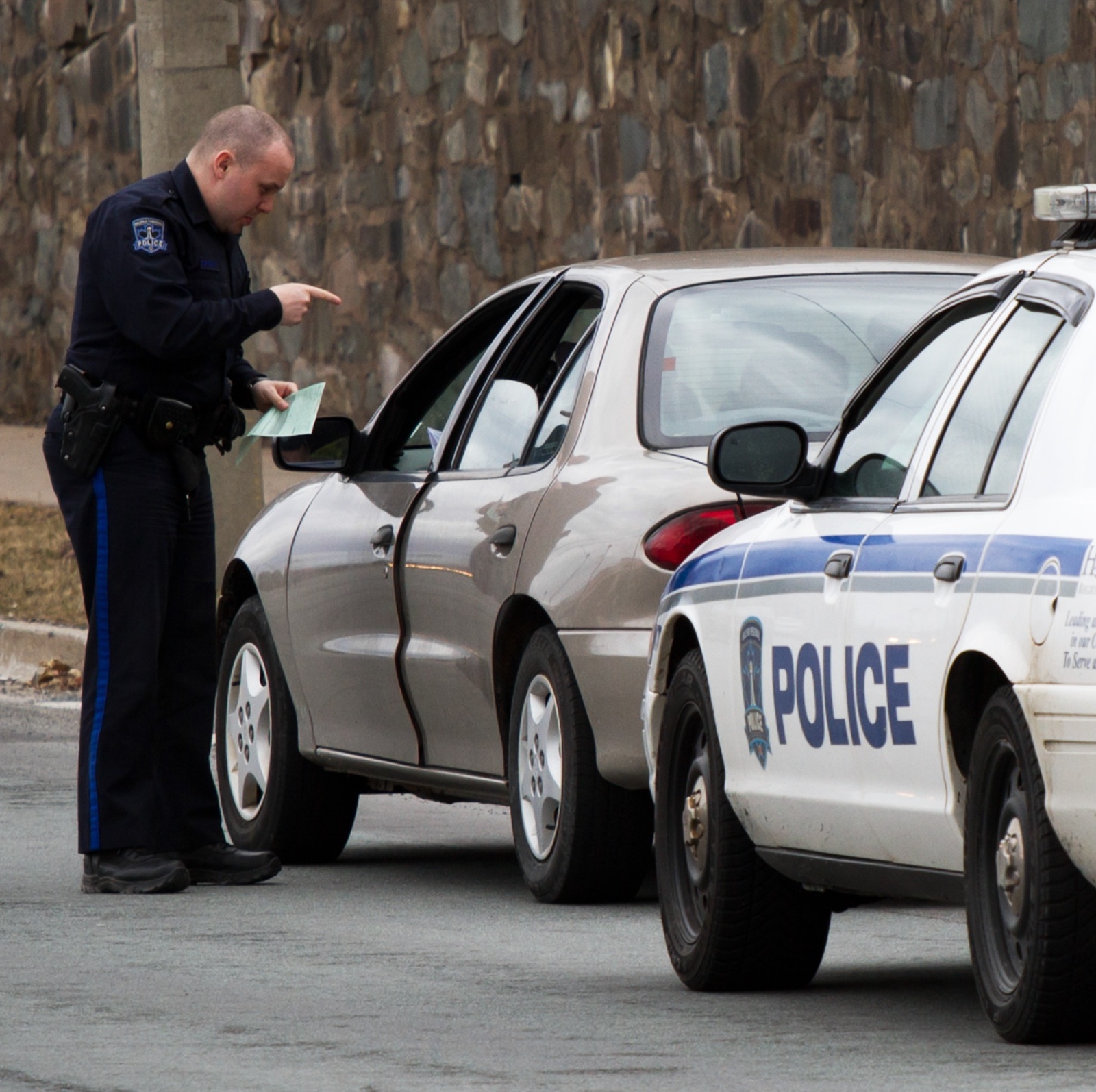 A fat bald police officer talking to a driver of a car he pulled over