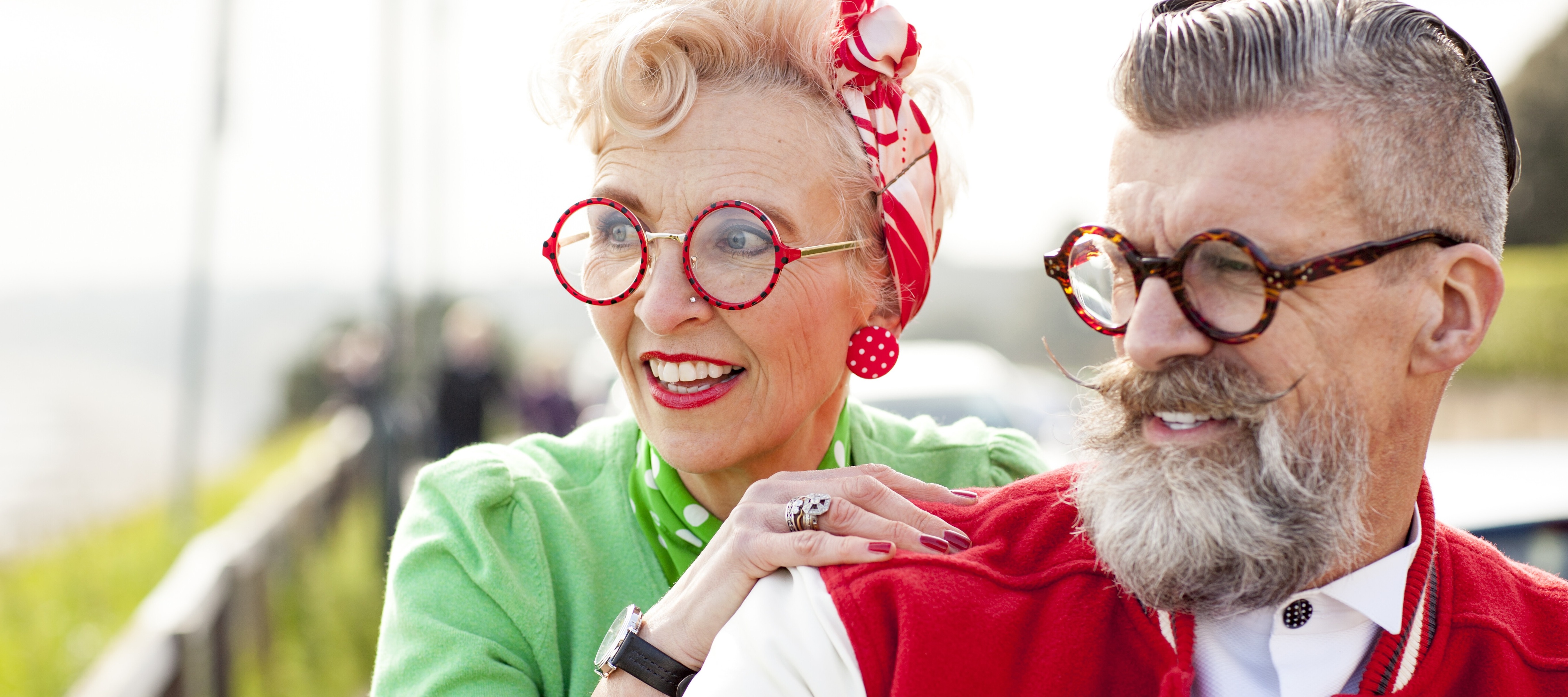 A joyful quirky older couple is captured in this vibrant waist-up shot, both smiling and looking off-camera with a lighthearted expression.