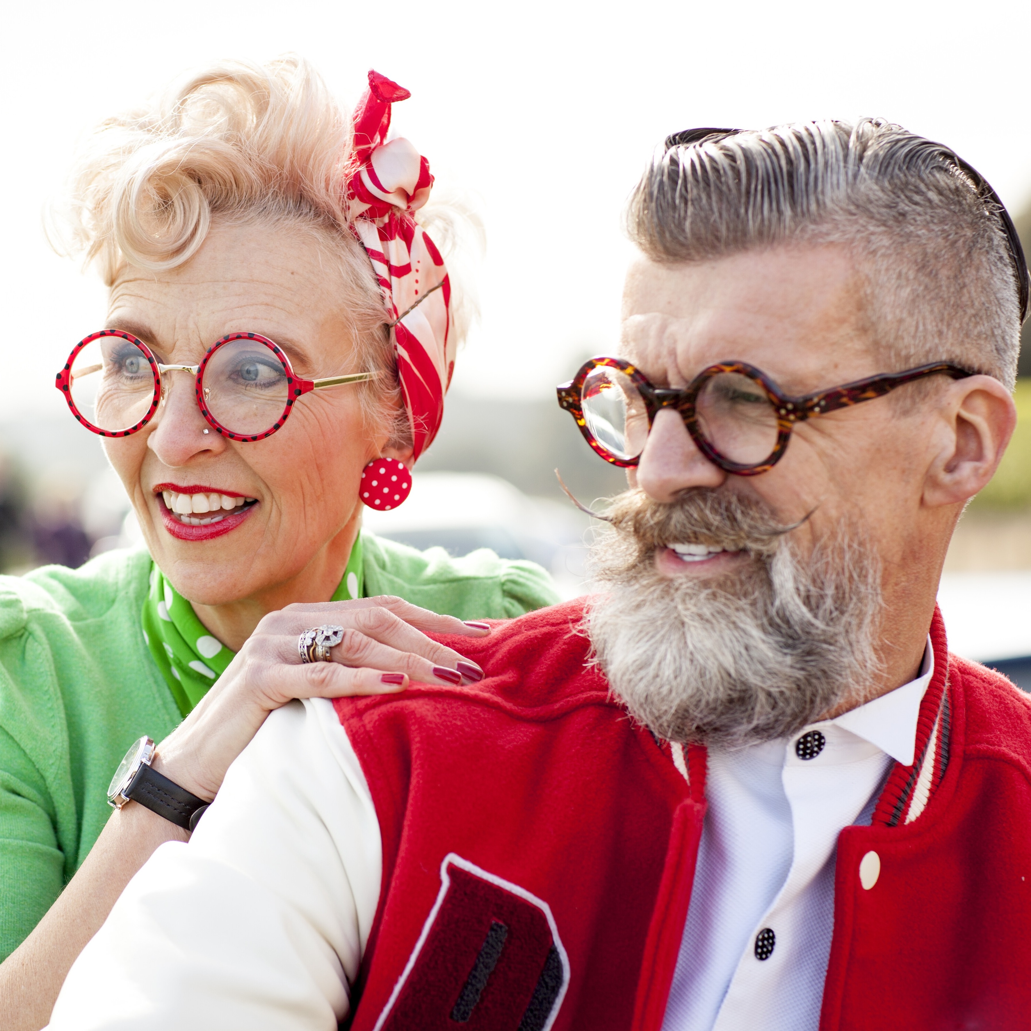A joyful quirky older couple is captured in this vibrant waist-up shot, both smiling and looking off-camera with a lighthearted expression.
