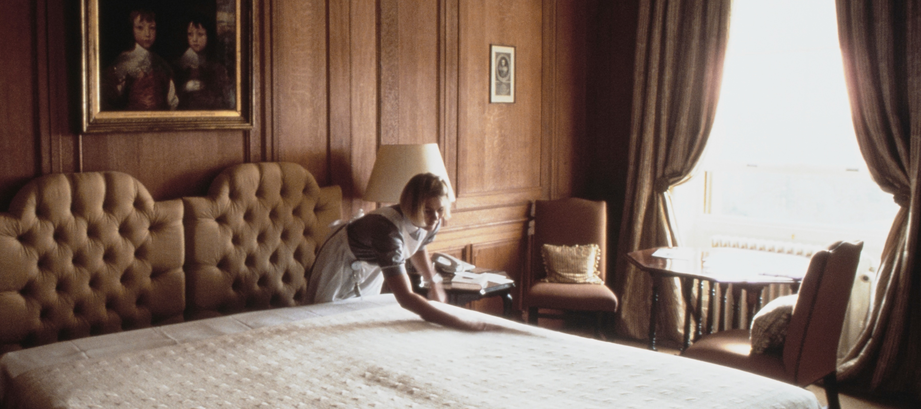 A maid, or housekeeper, making a bed in a luxurious bedroom