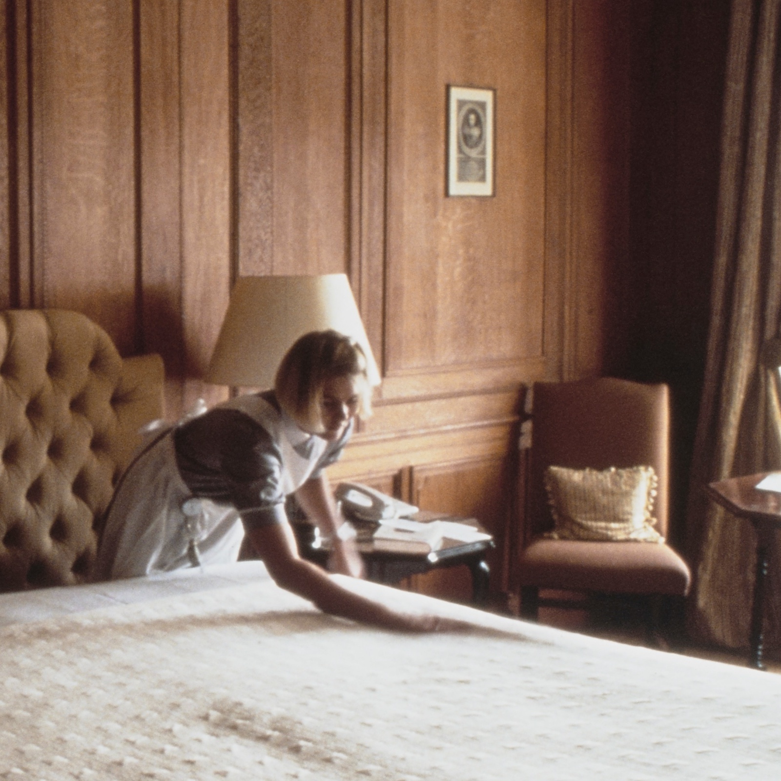 A maid, or housekeeper, making a bed in a luxurious bedroom