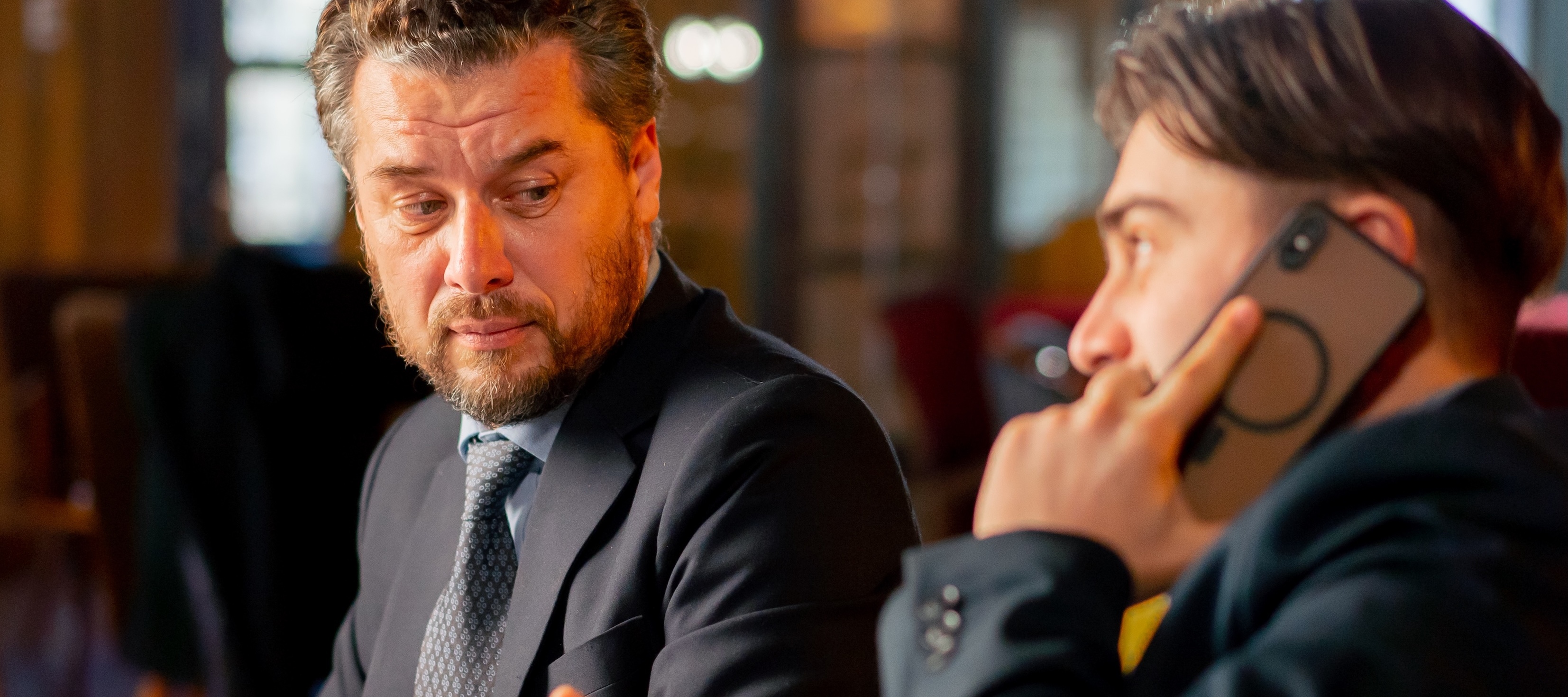 two men in suits. One is on the phone while the other stares at him