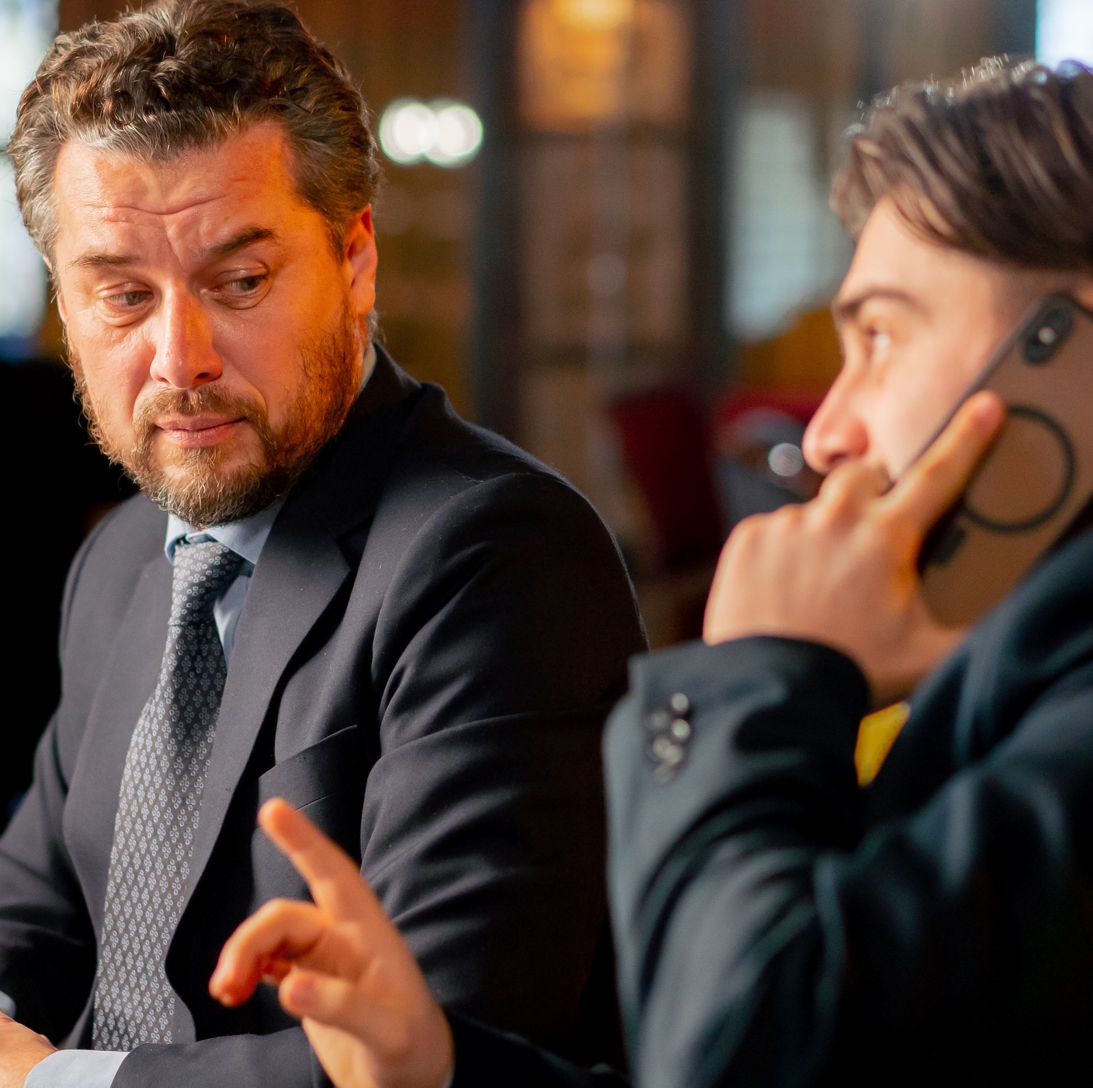 two men in suits. One is on the phone while the other stares at him