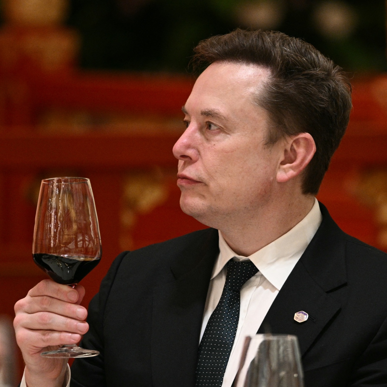 A collage image of a Space X rocket taking flight and Elon Musk holding up a glass of red wine as if toasting a success.