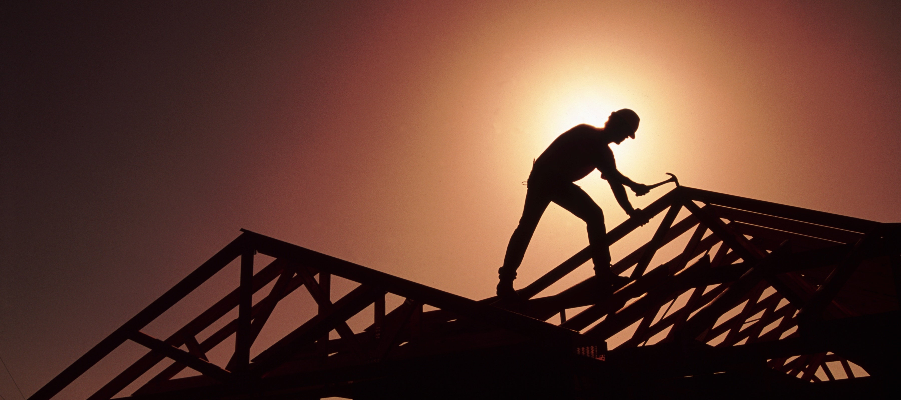 A silhouette of a homebuilder working on a roof