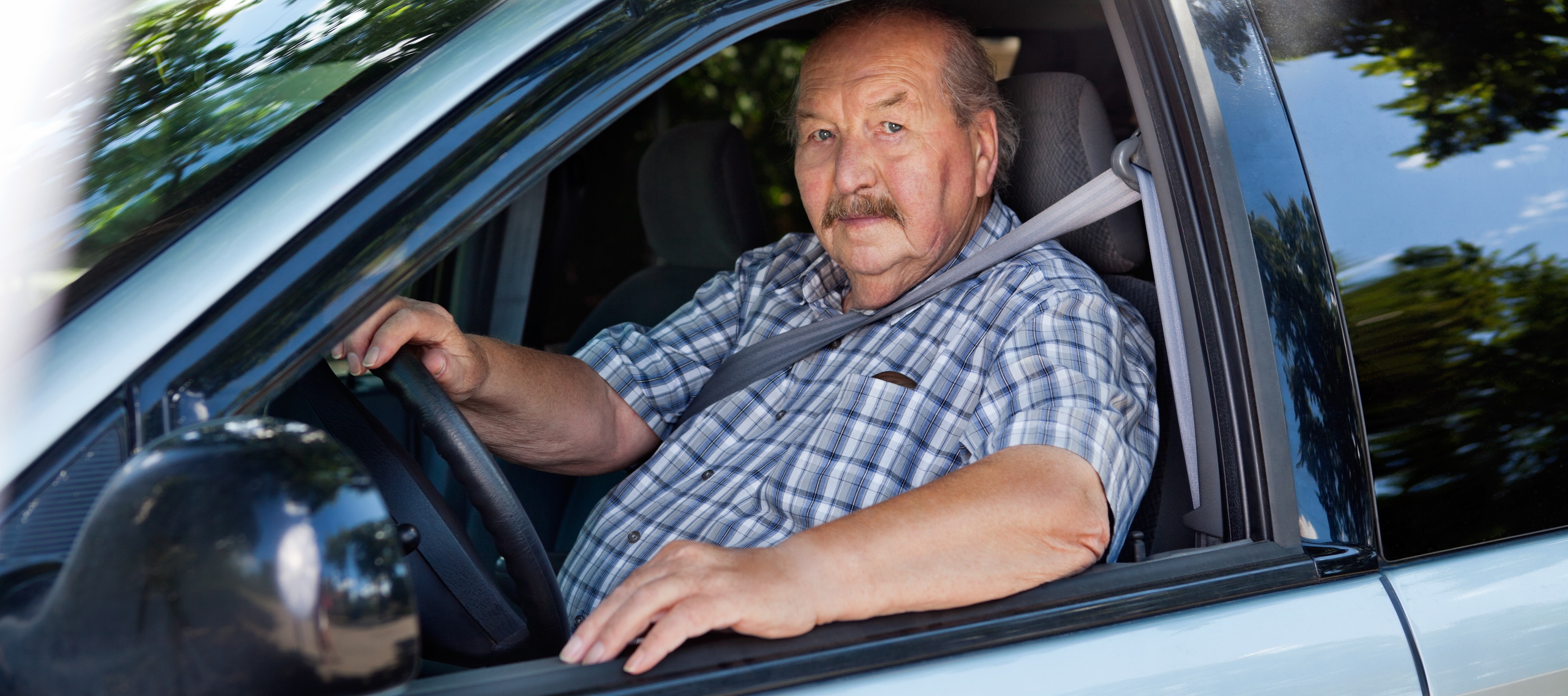 Portrait of an older gentleman driving a mid-range, older model car.