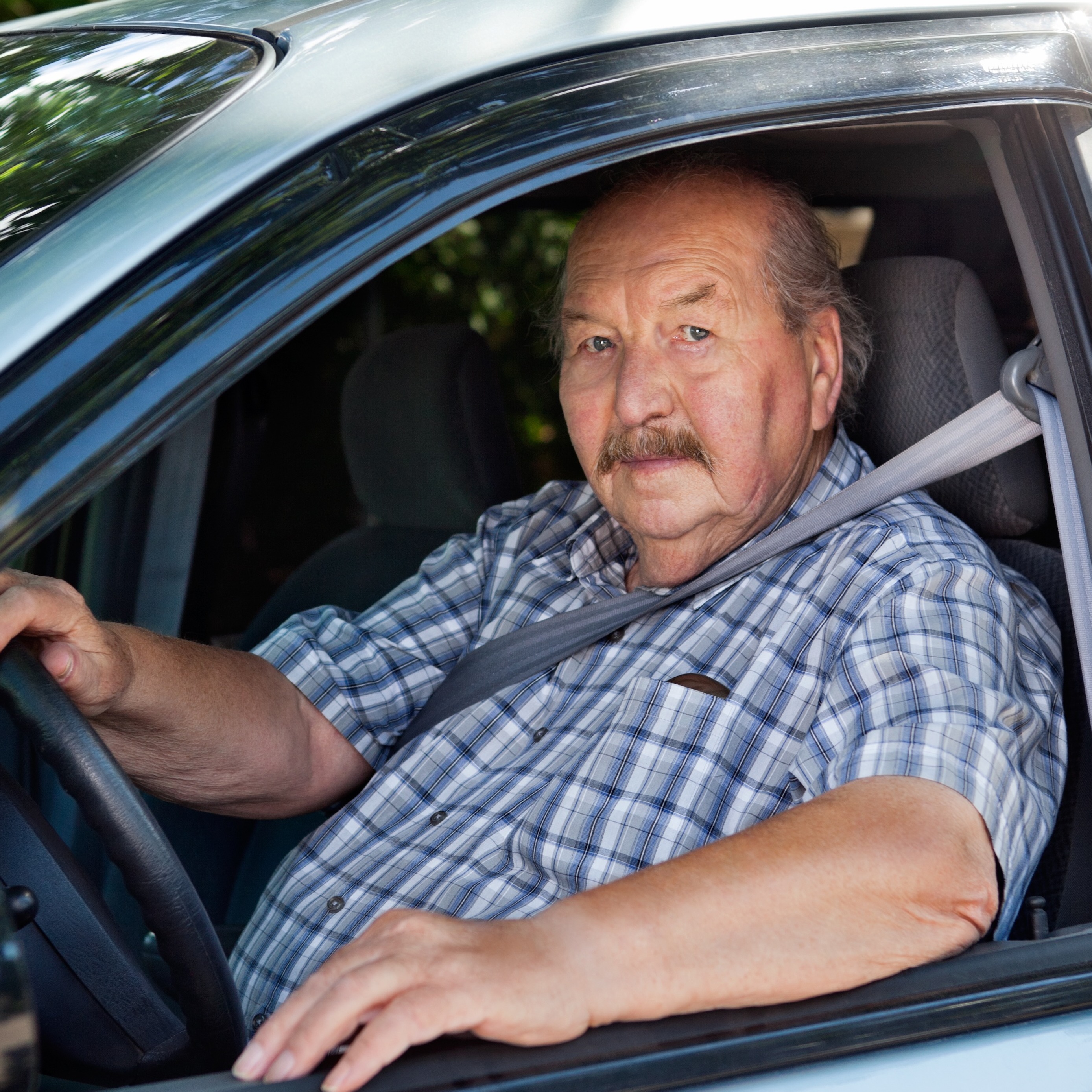 Portrait of an older gentleman driving a mid-range, older model car.