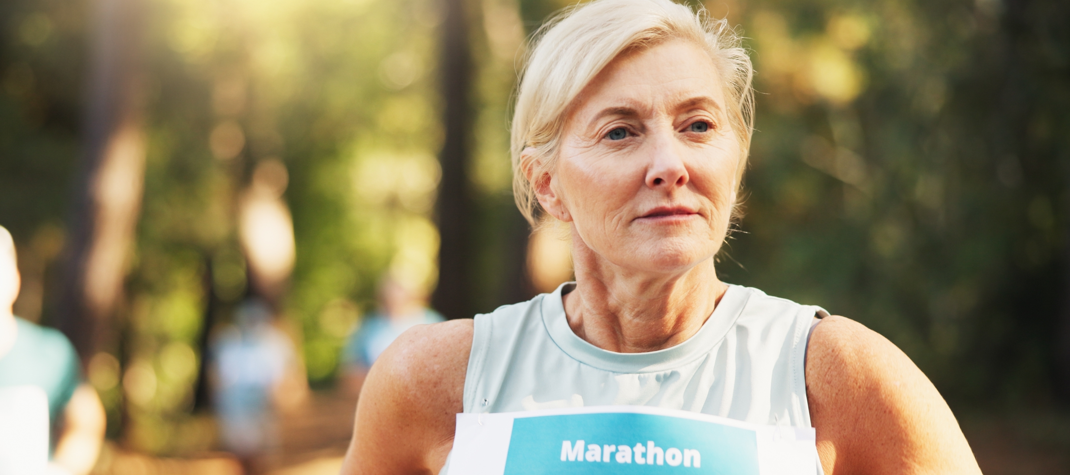 An older blonde woman runs a marathon confidently with a blurry pack of other runners far behind.