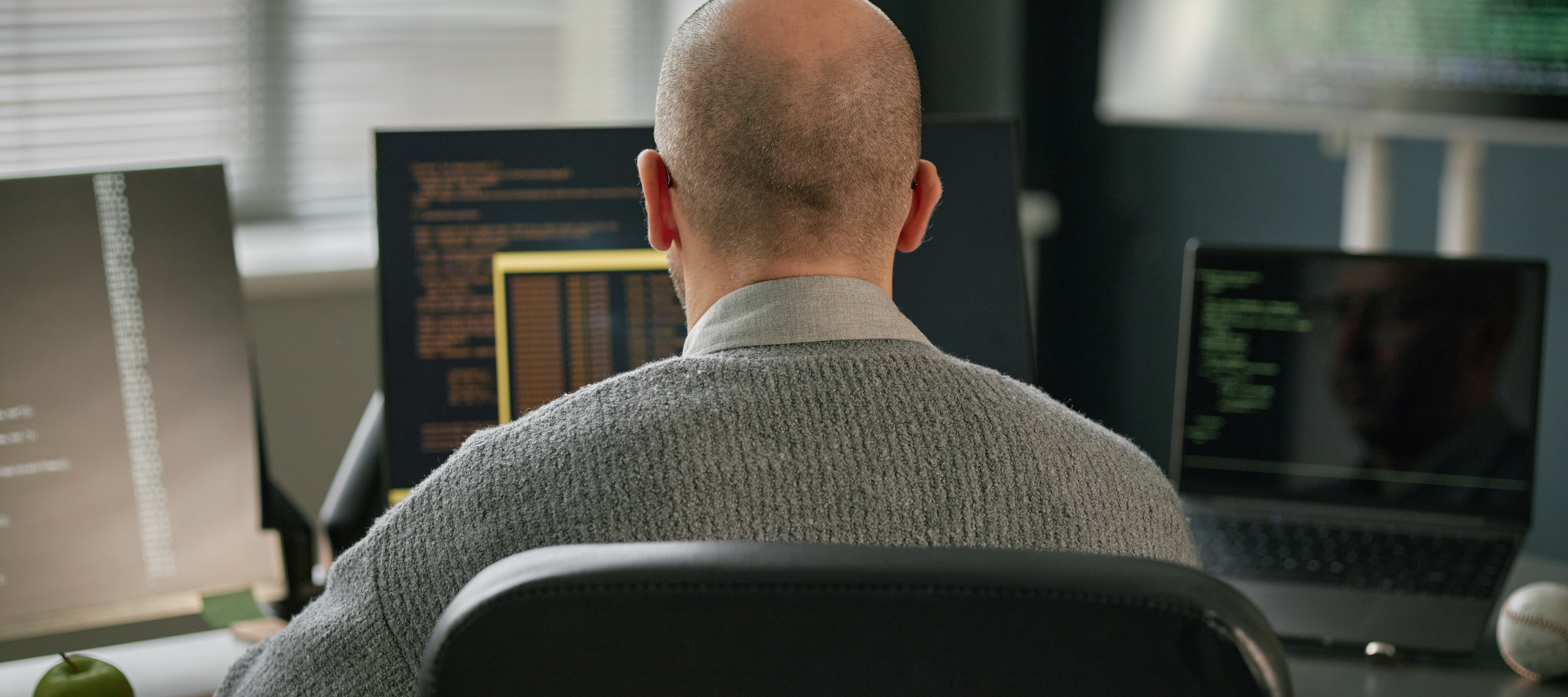 A man tends to his job using multiple computer screens.